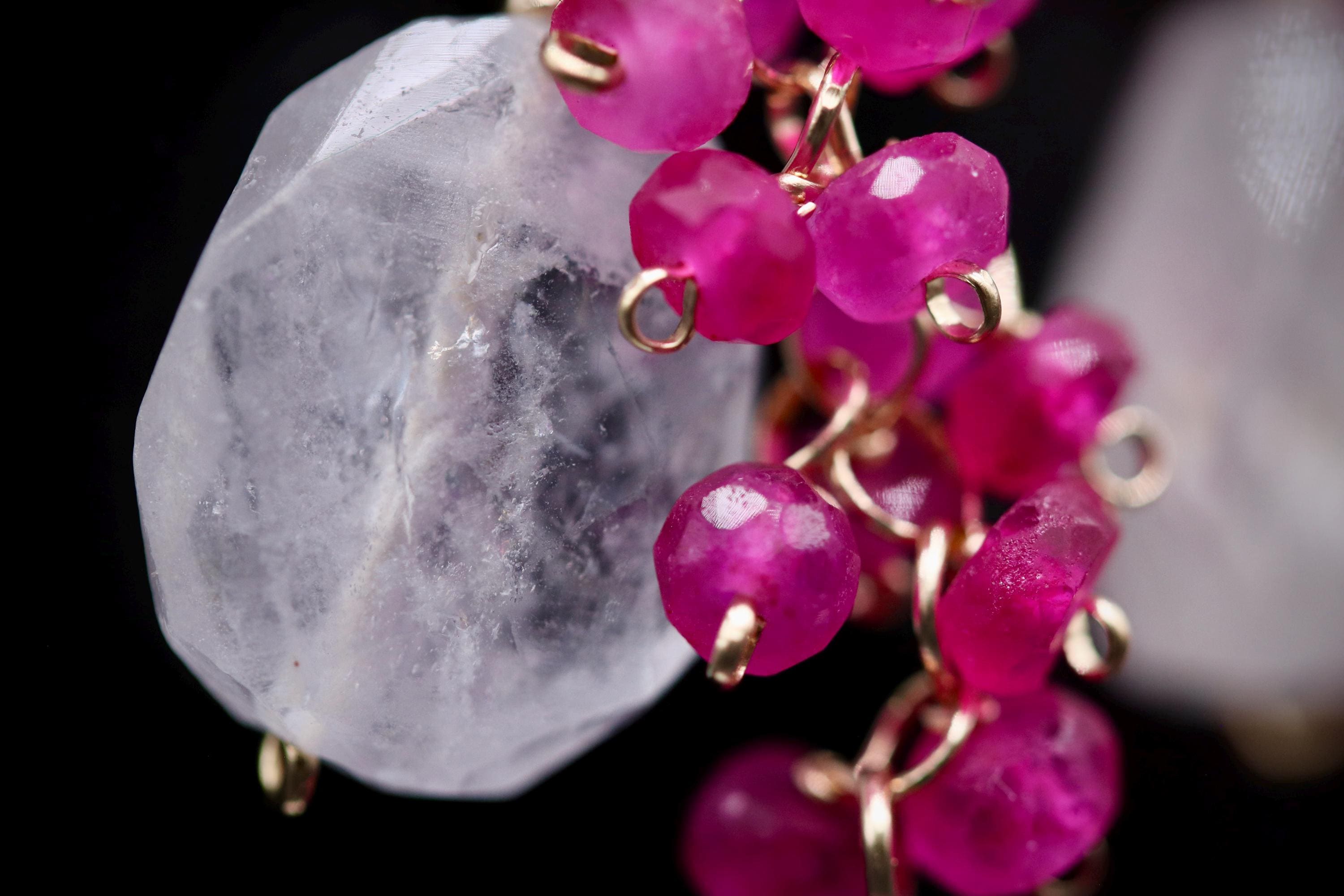 A close-up image of a piece of jewelry with a clear crystal and a cluster of pink gemstones, including amethyst and jade beads.