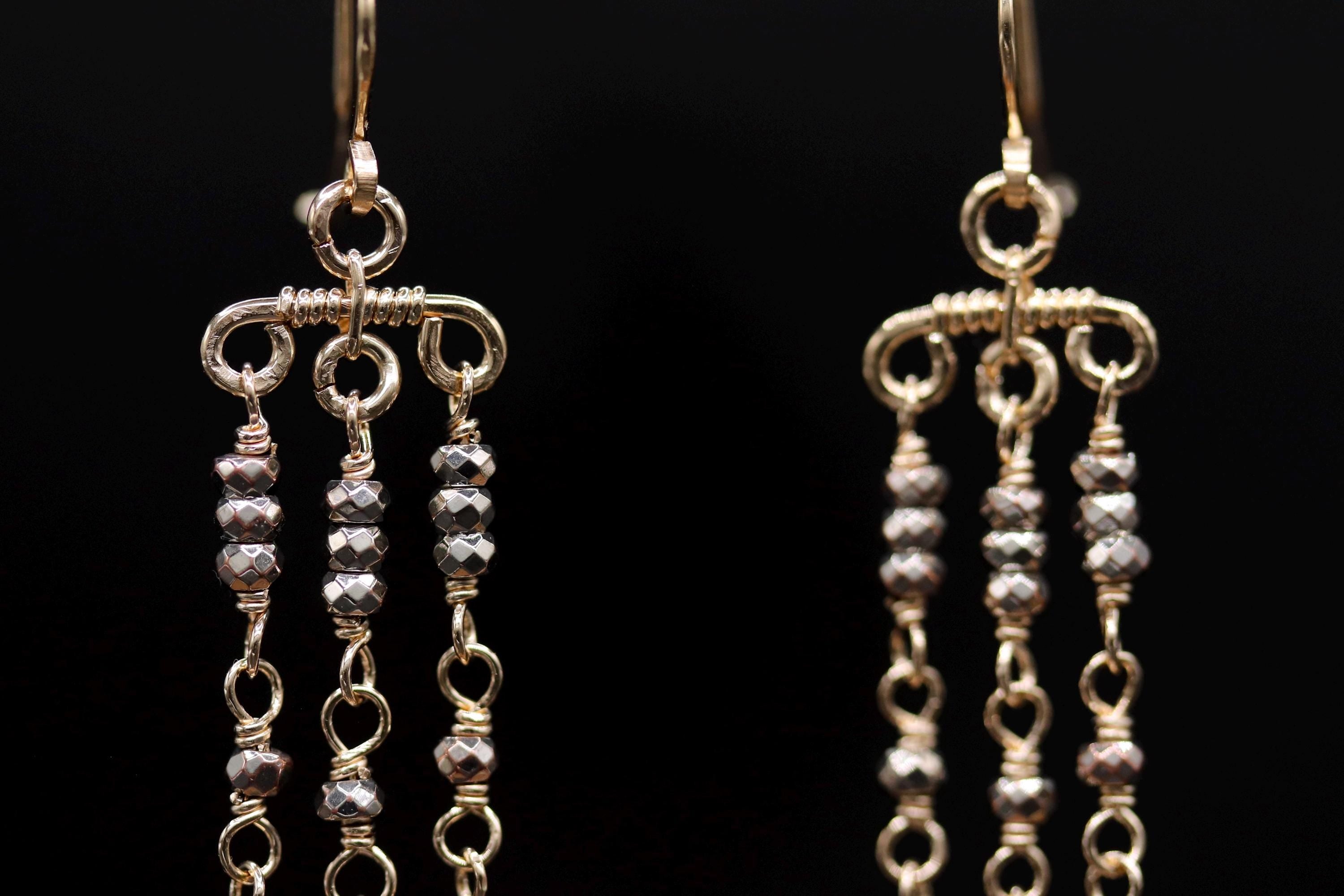 A close-up view of a pair of gold-colored earrings with multiple tiers of dangling beads.