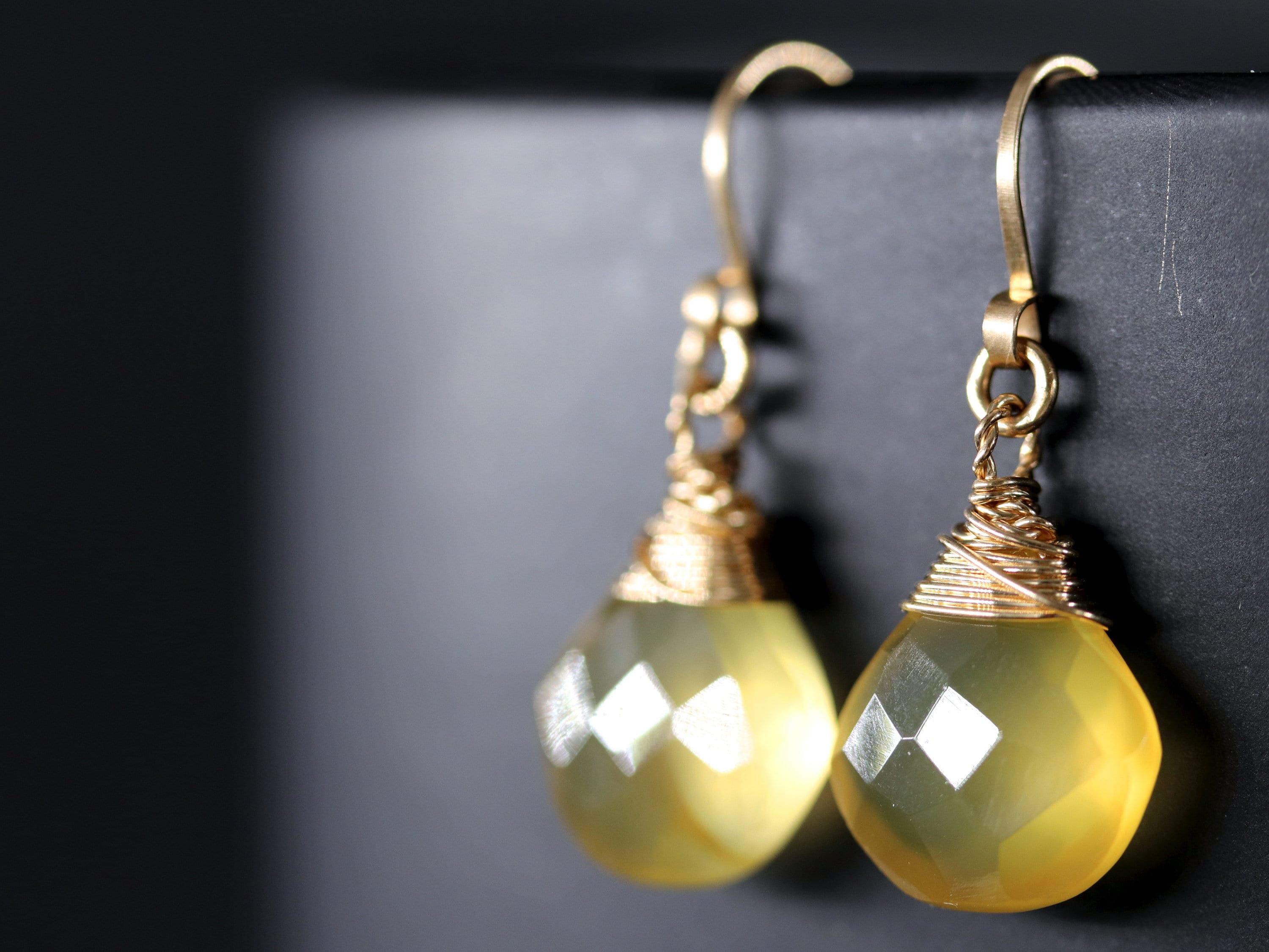 May include: A pair of gold earrings with yellow teardrop-shaped stones wrapped in gold wire.