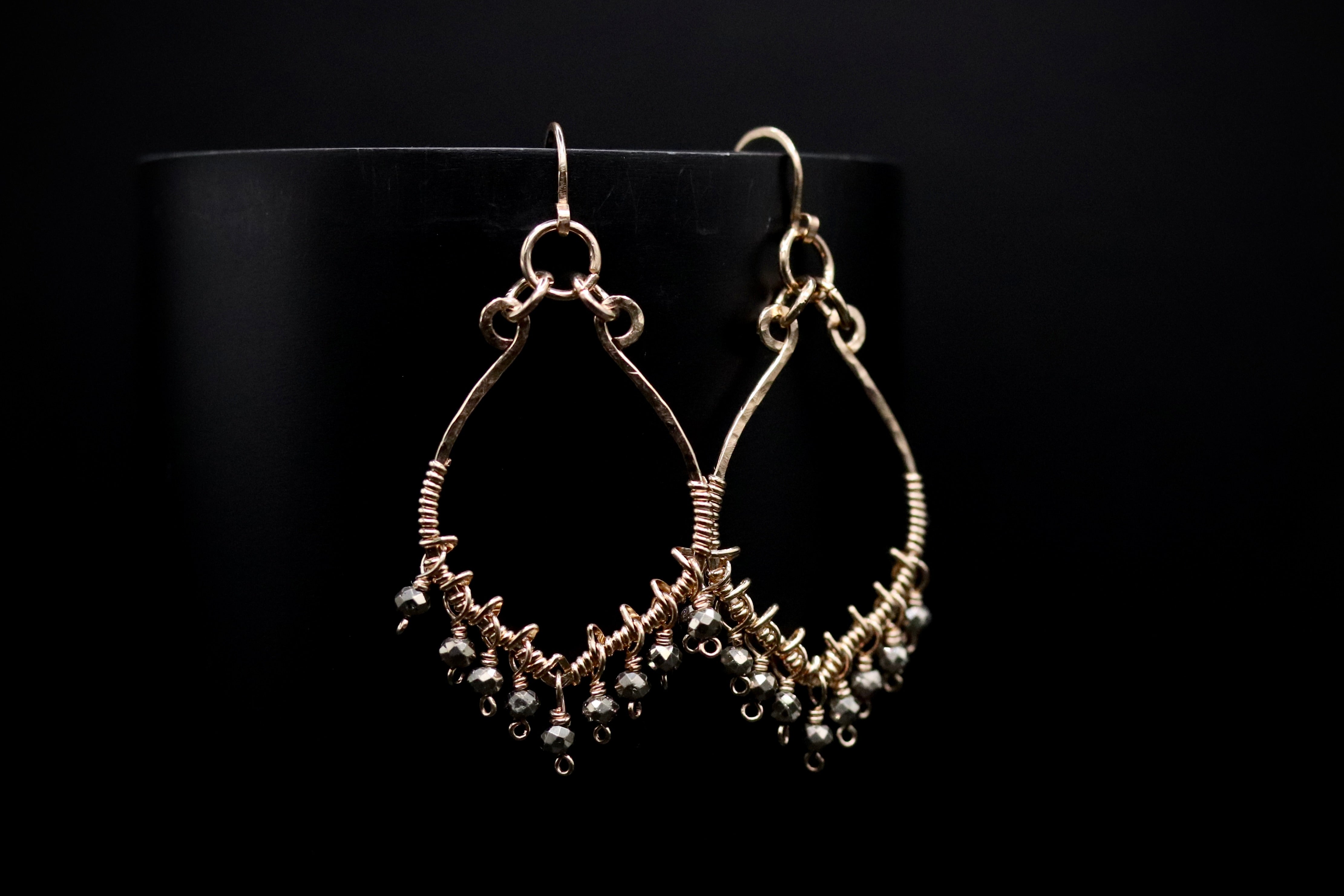 A pair of gold earrings with dangling beads against a black background.