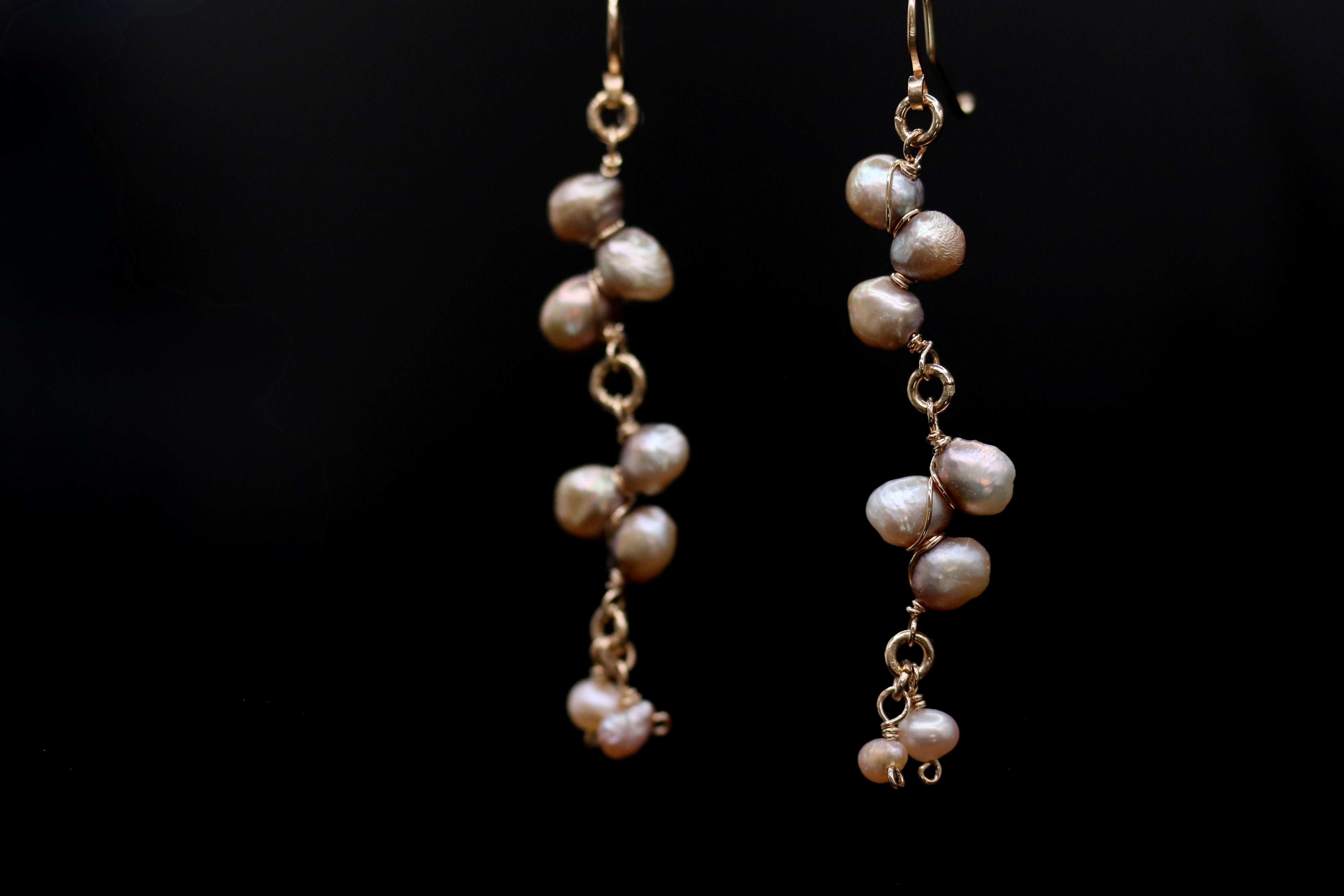 A pair of elegant earrings with a delicate chain design, featuring a cluster of small, round pearls suspended from the chain.