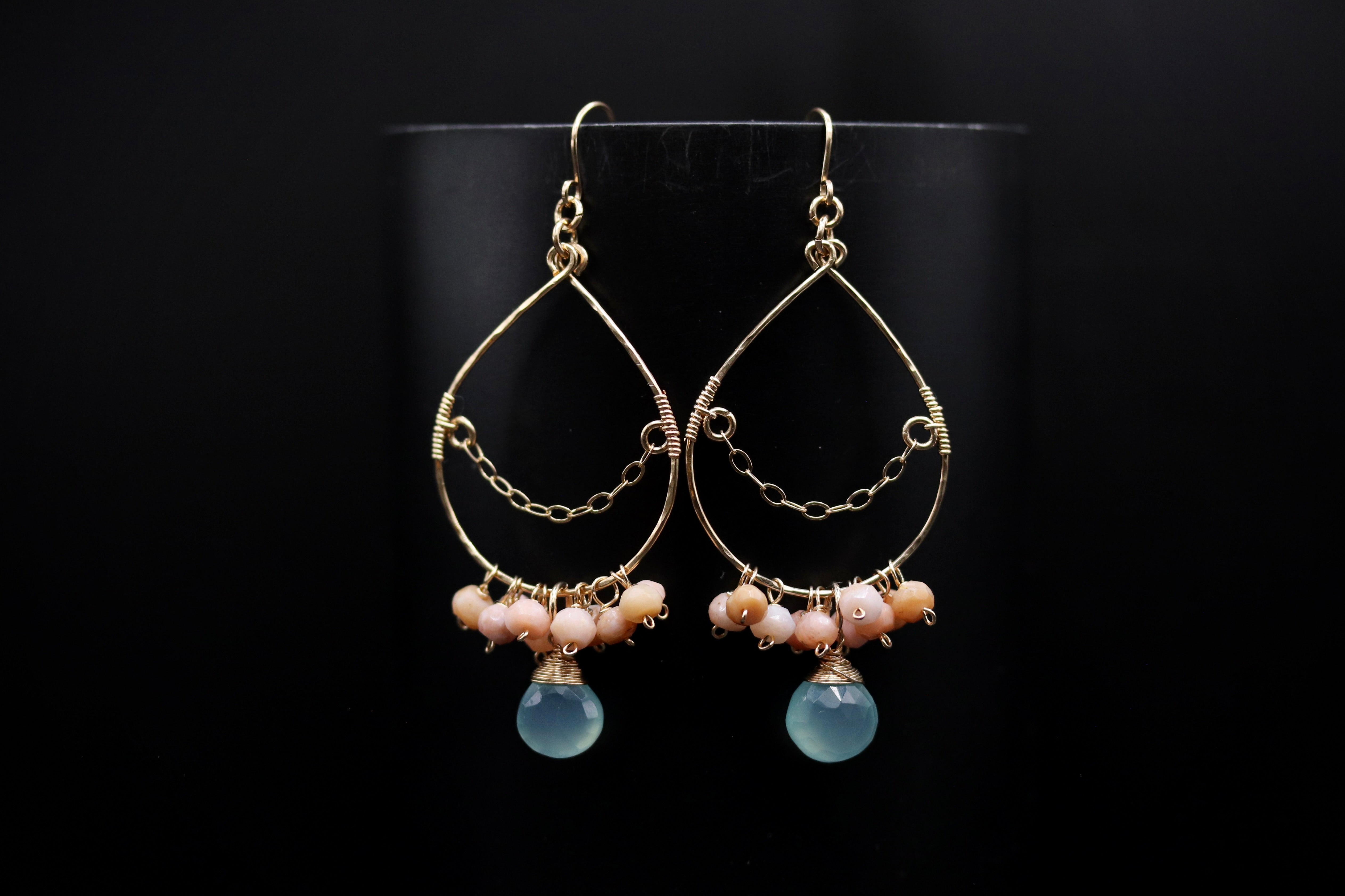 A pair of gold earrings with blue and pink stones hanging from them, set against a black background.