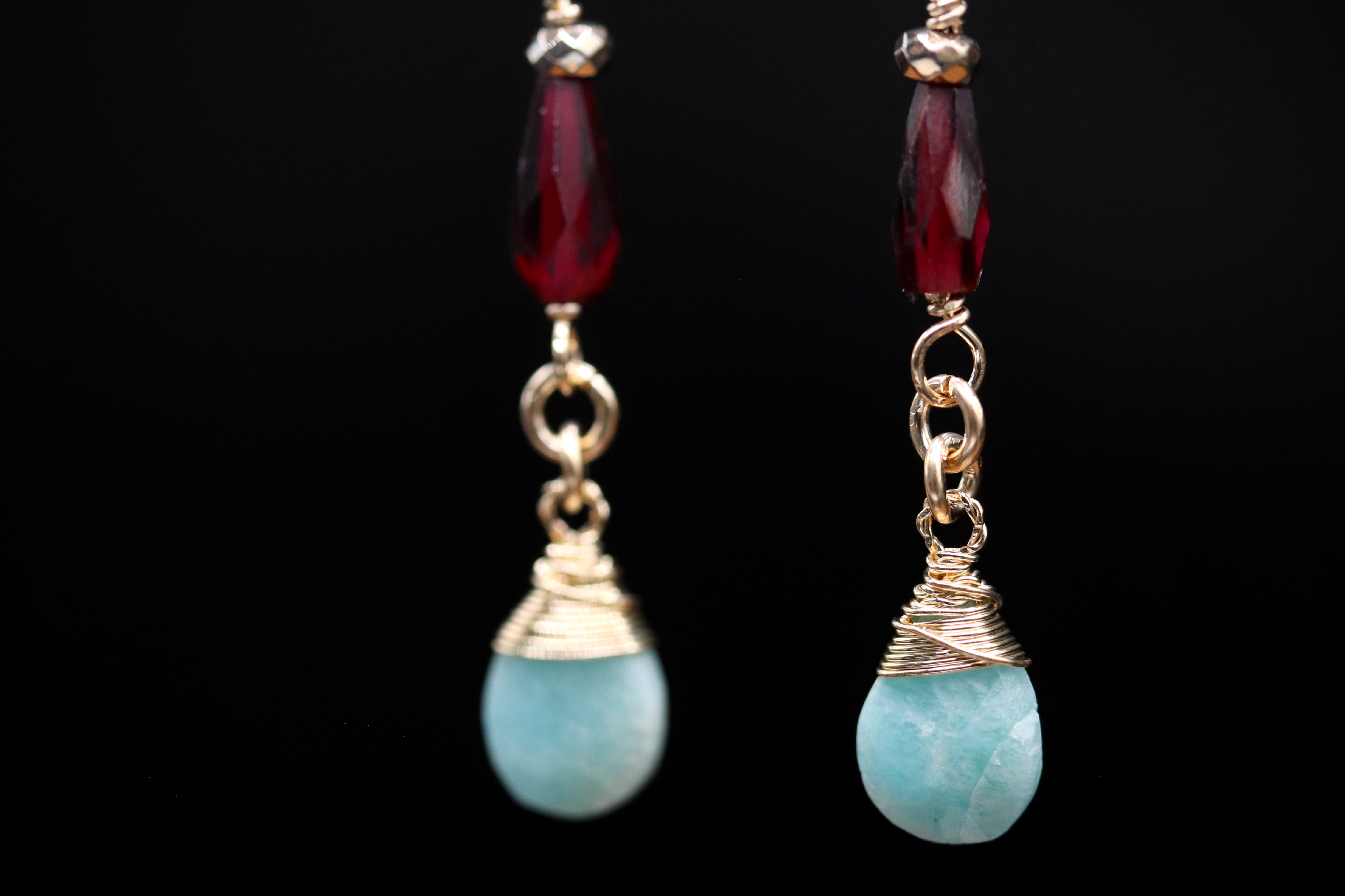 A pair of earrings with turquoise stones and red gemstones, suspended from gold chains against a black background.