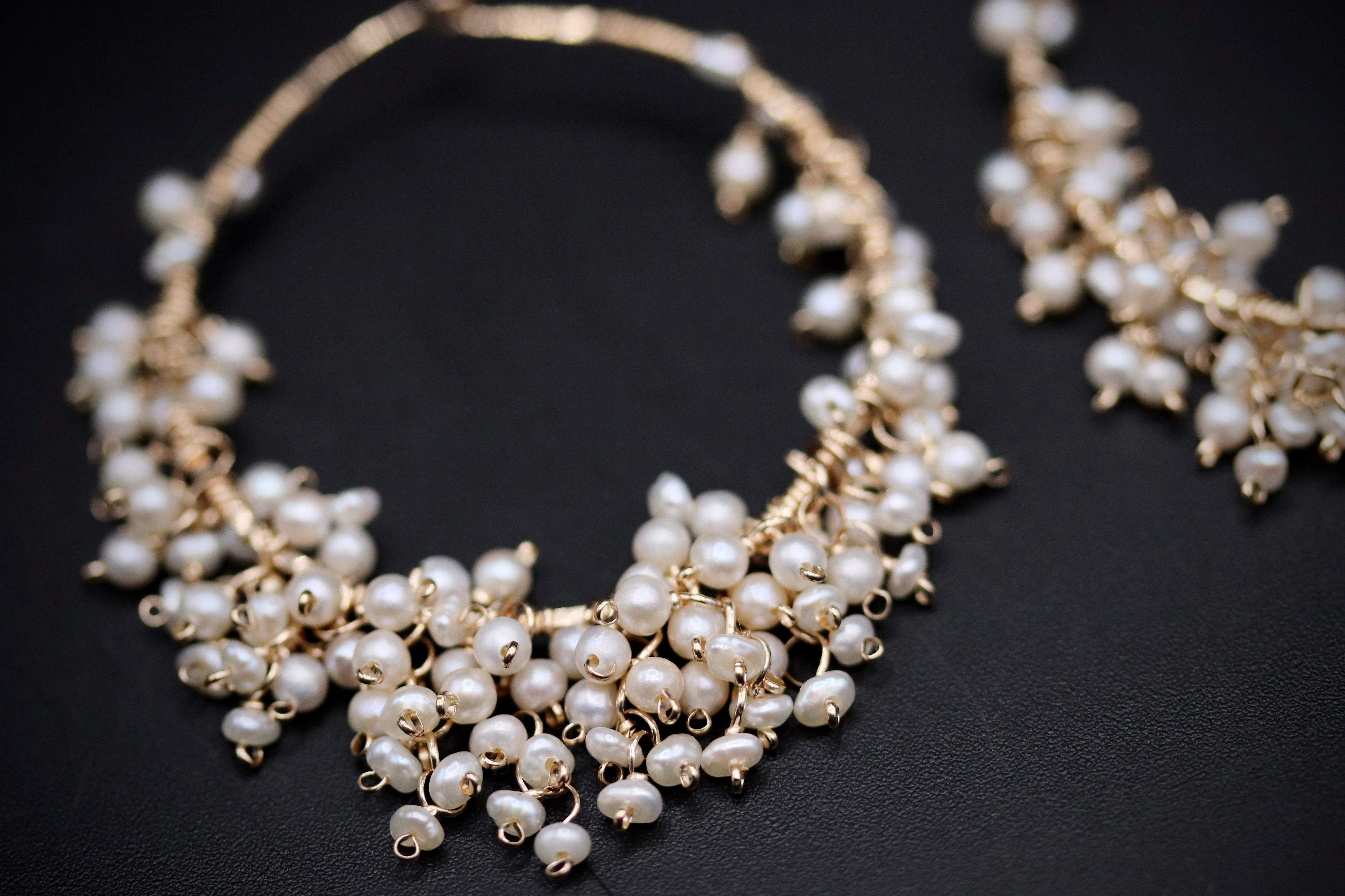 A close-up image of a delicate, ornate necklace with numerous small, white pearls arranged in a decorative pattern.