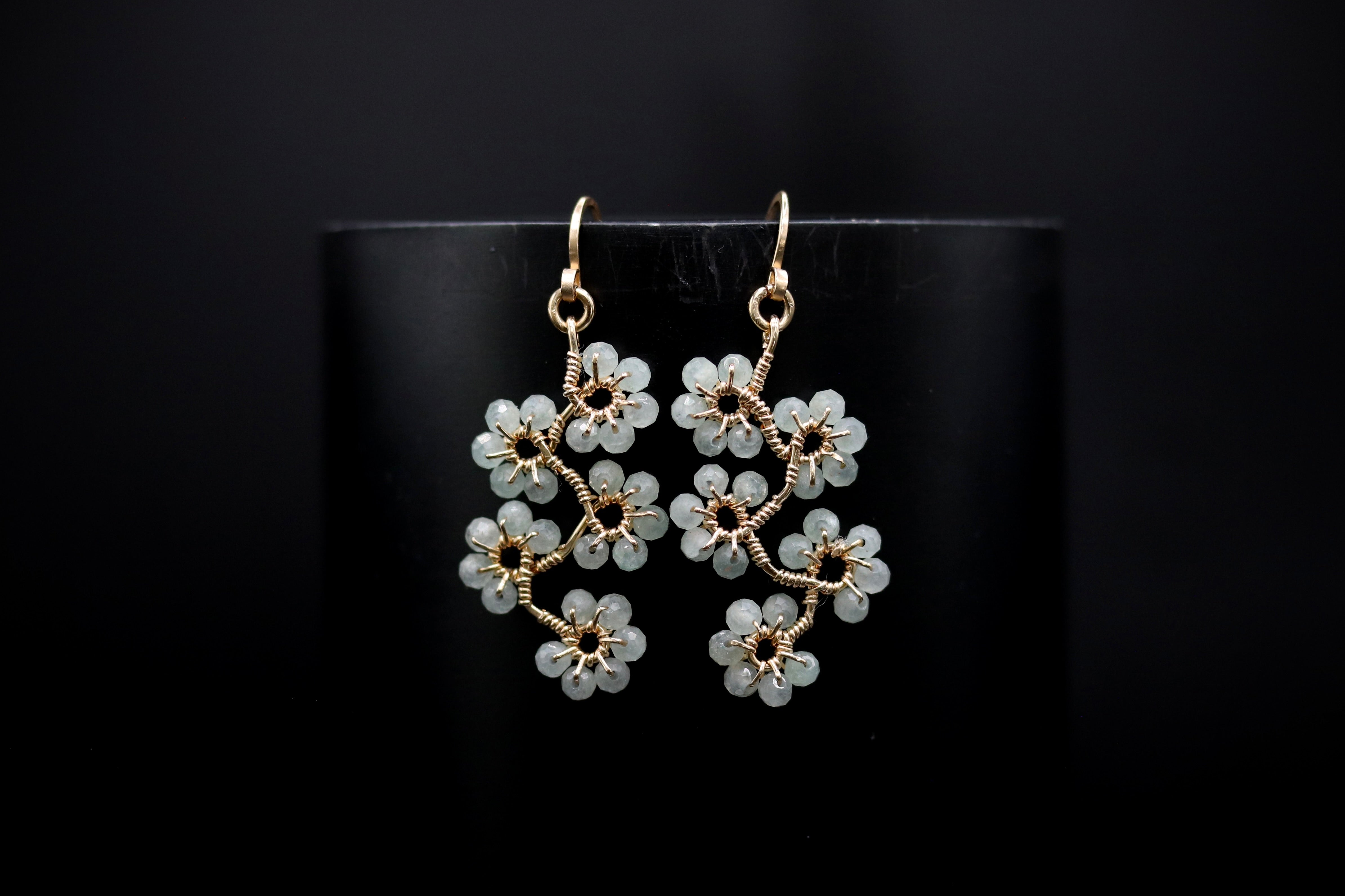 A pair of elegant earrings with delicate white flower-like designs, displayed against a dark background.