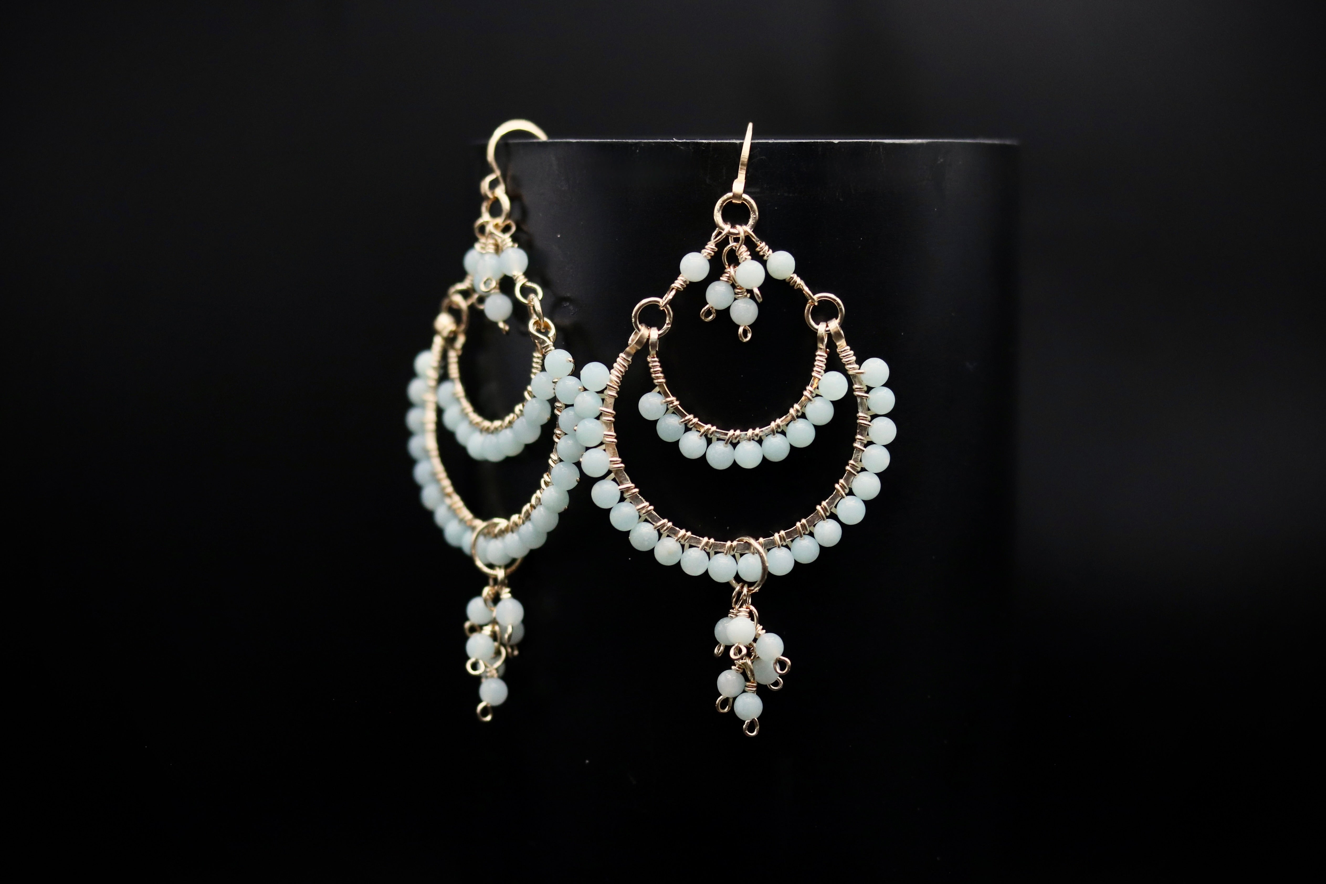 A pair of elegant earrings with white beads and dangling charms, displayed against a black background.