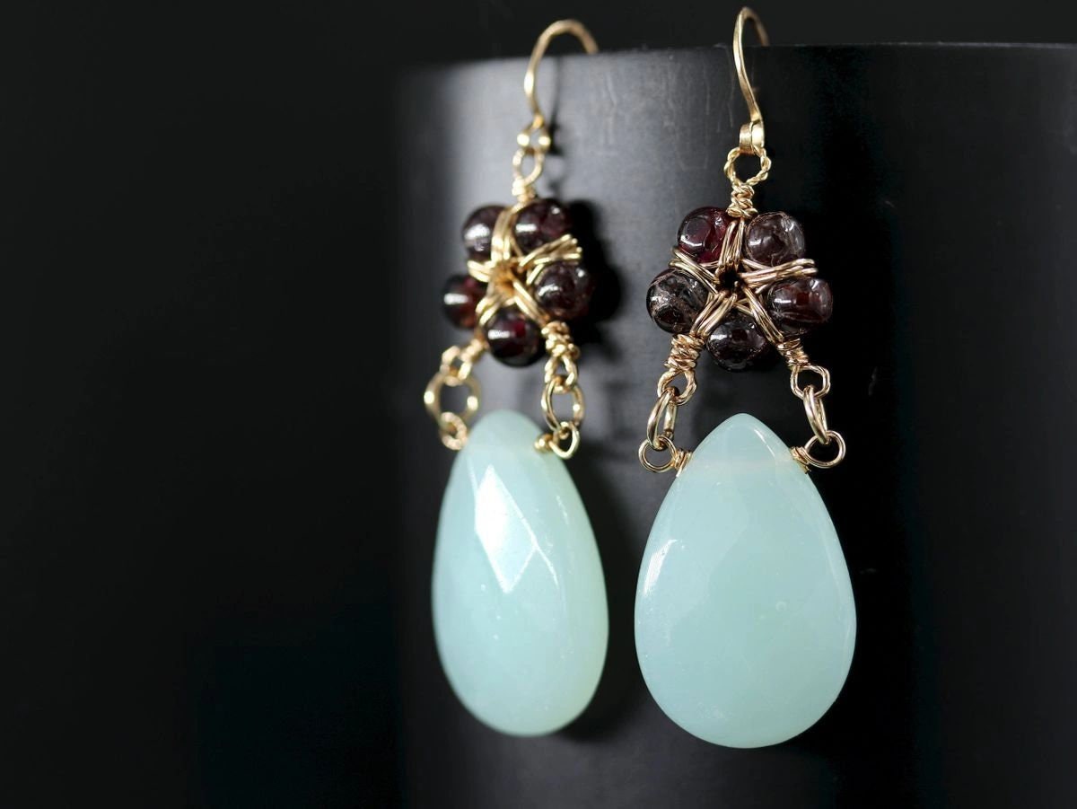May include: Gold earrings with teardrop-shaped light blue gemstones and a cluster of dark red beads.