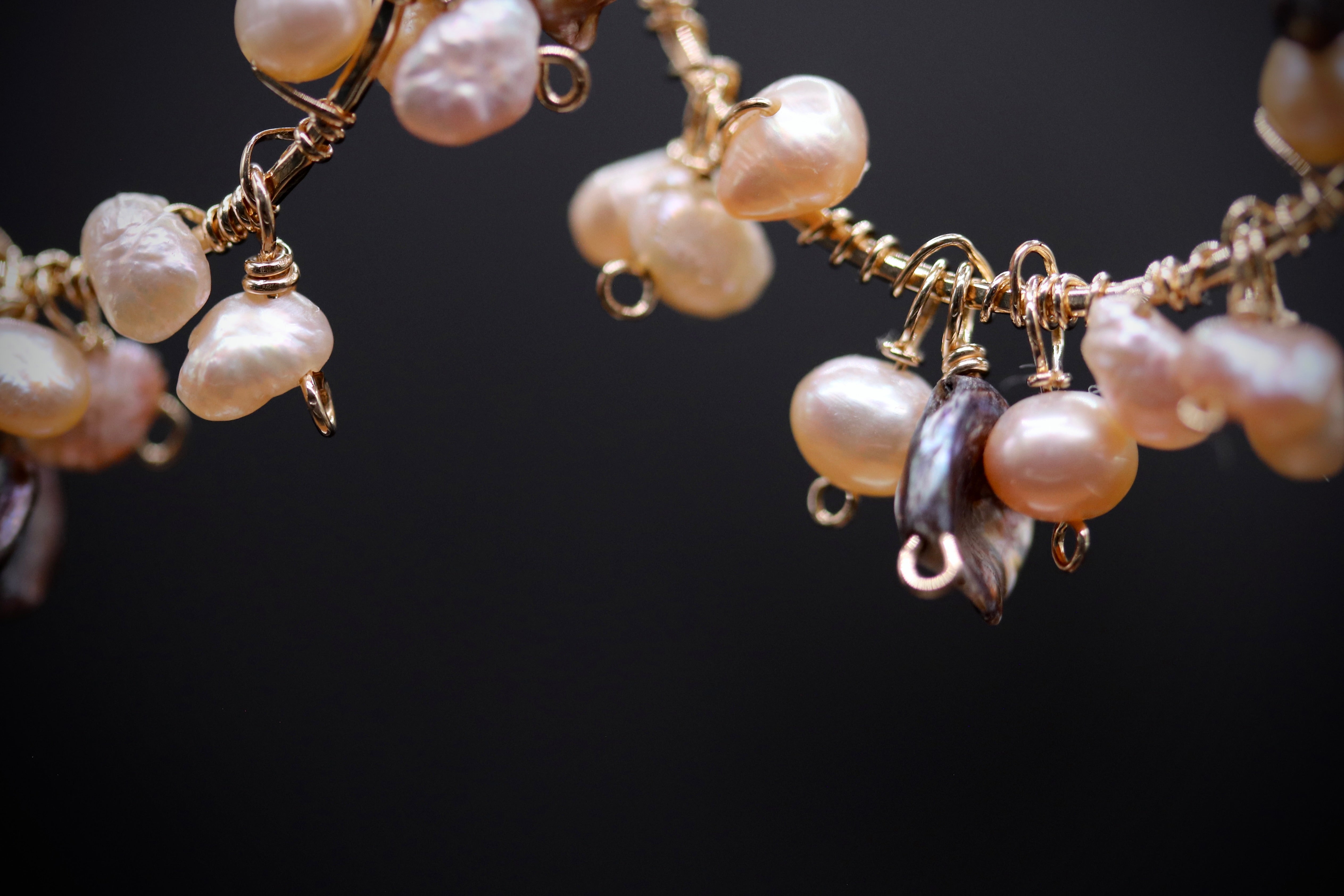 A close-up view of a delicate necklace with a variety of pearls and charms, including white, pink, and brown pearls, as well as some dangling charms.