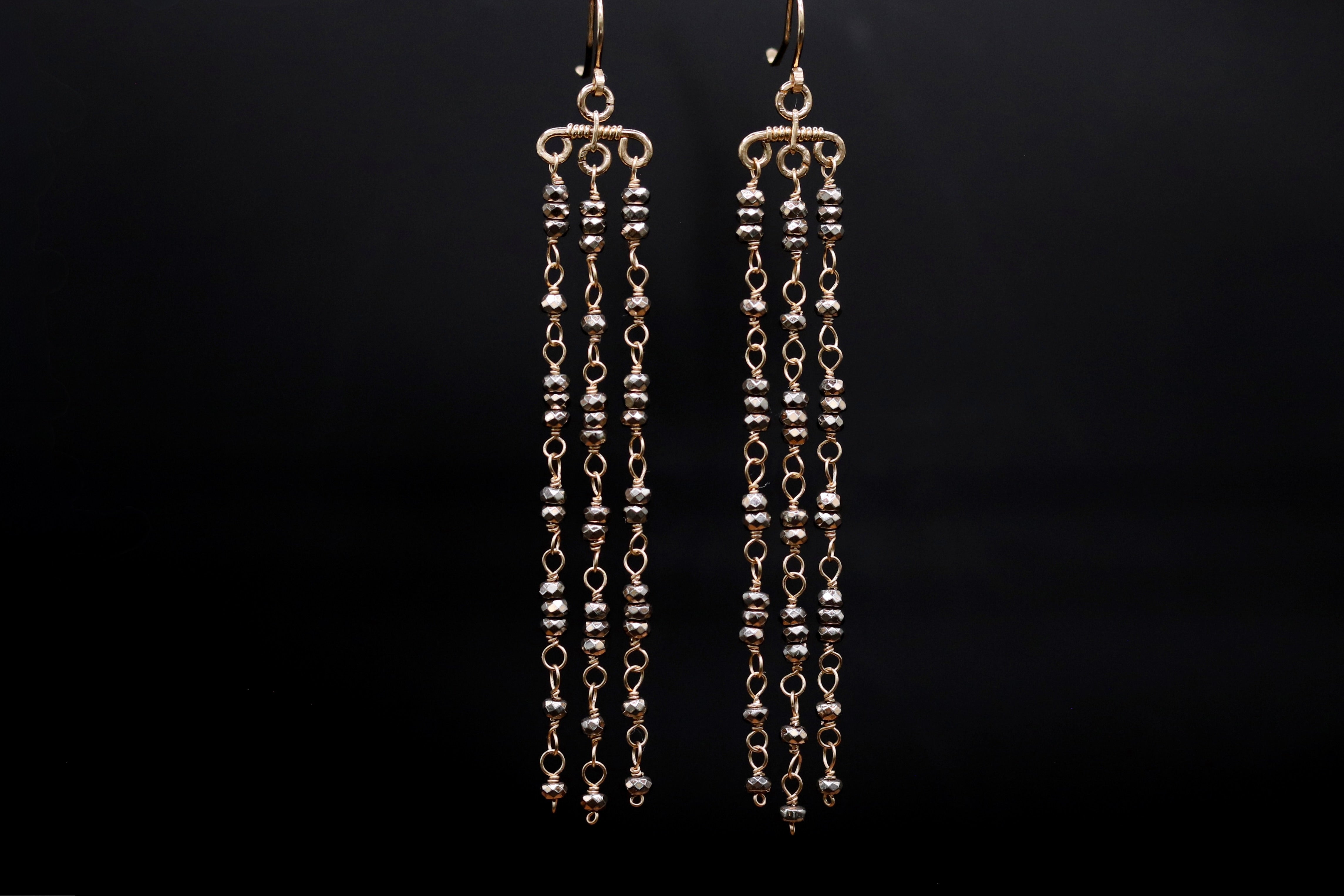 A pair of gold earrings with long, dangling chains and small, round beads hanging from them.
