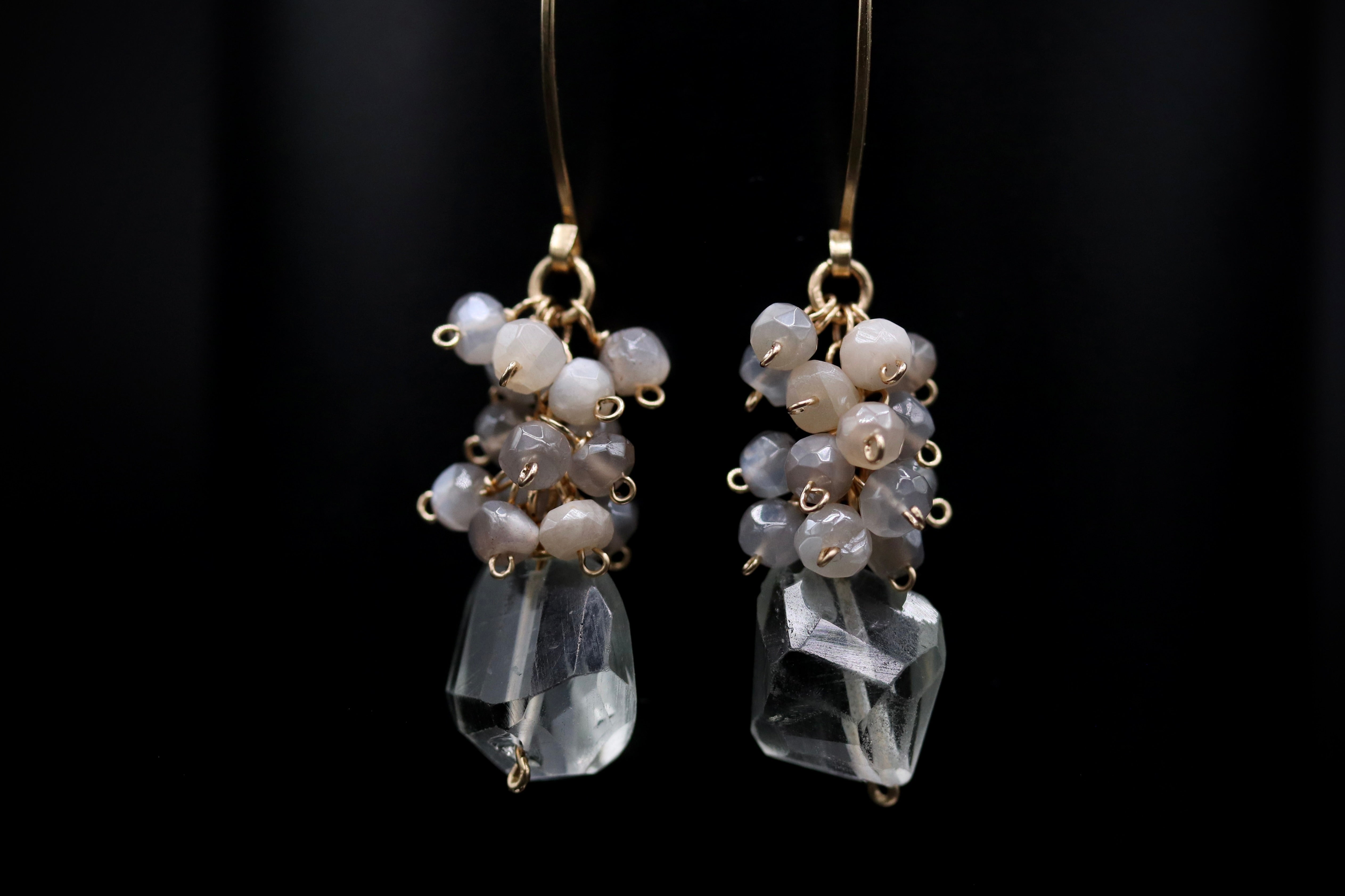 A pair of elegant earrings with clear gemstone accents and dangling metal chains against a dark background.