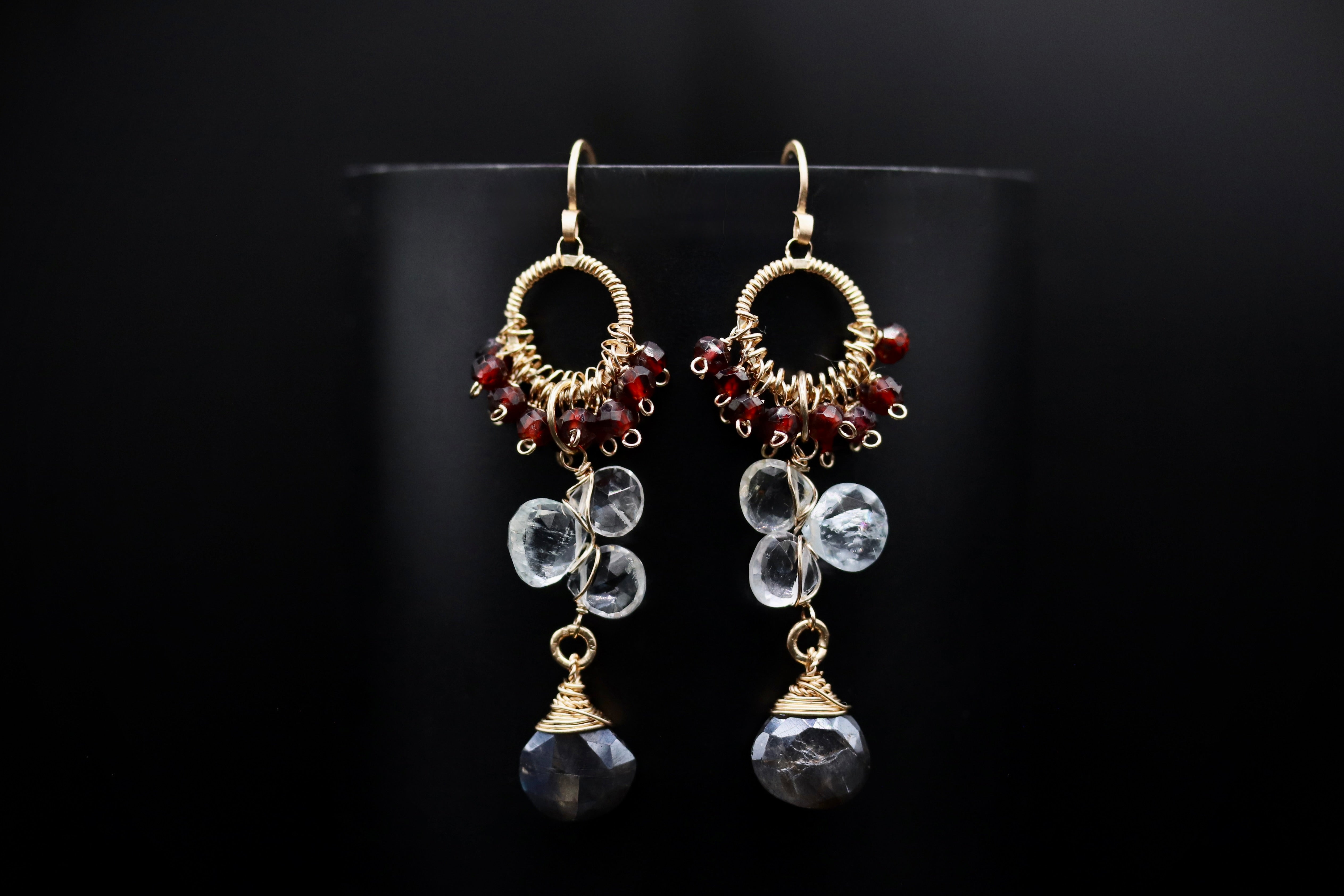 A pair of elegant earrings with a combination of clear gemstones and metallic beads, set against a black background.