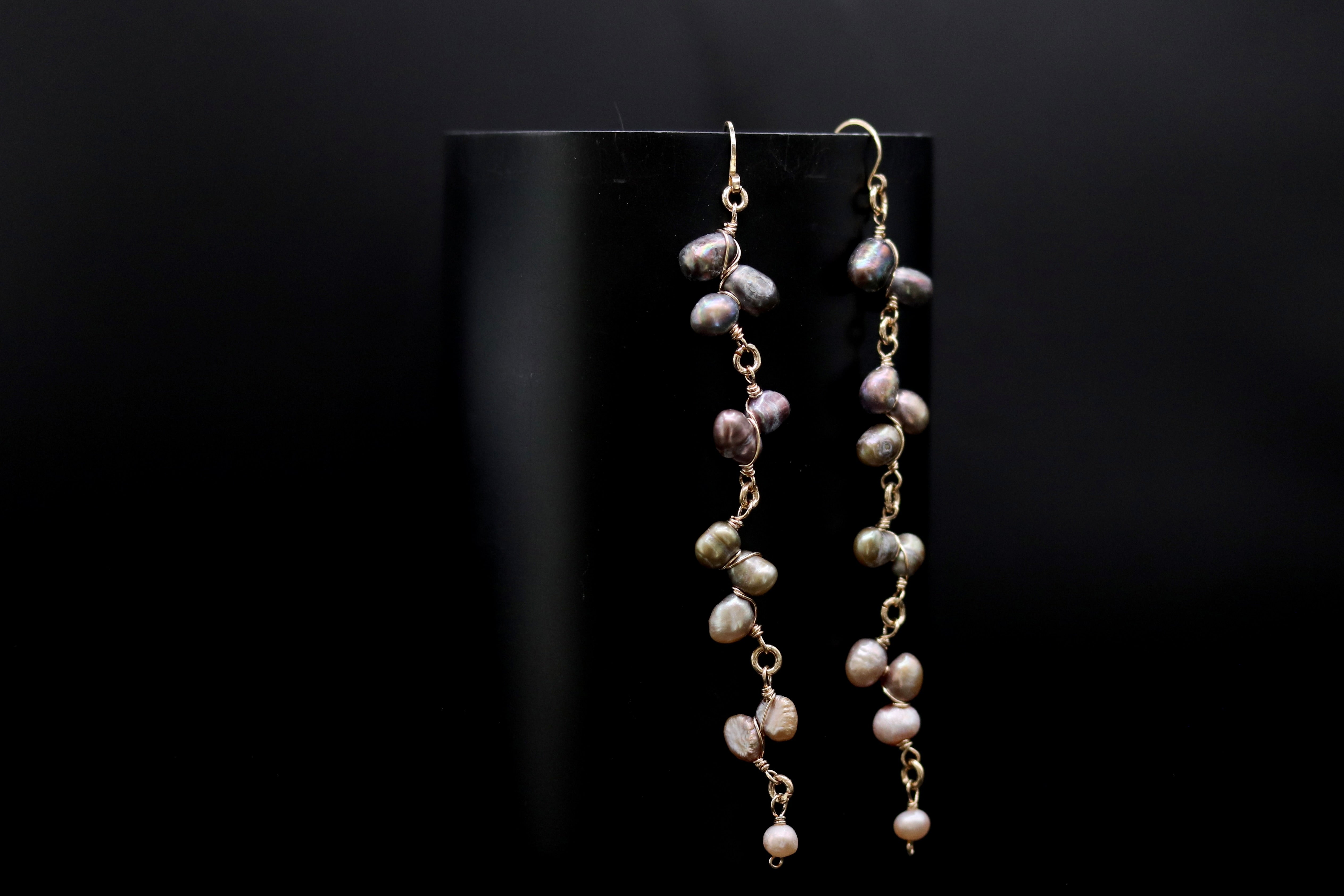 A pair of earrings with a black background and a row of pearls hanging from the ear hooks.