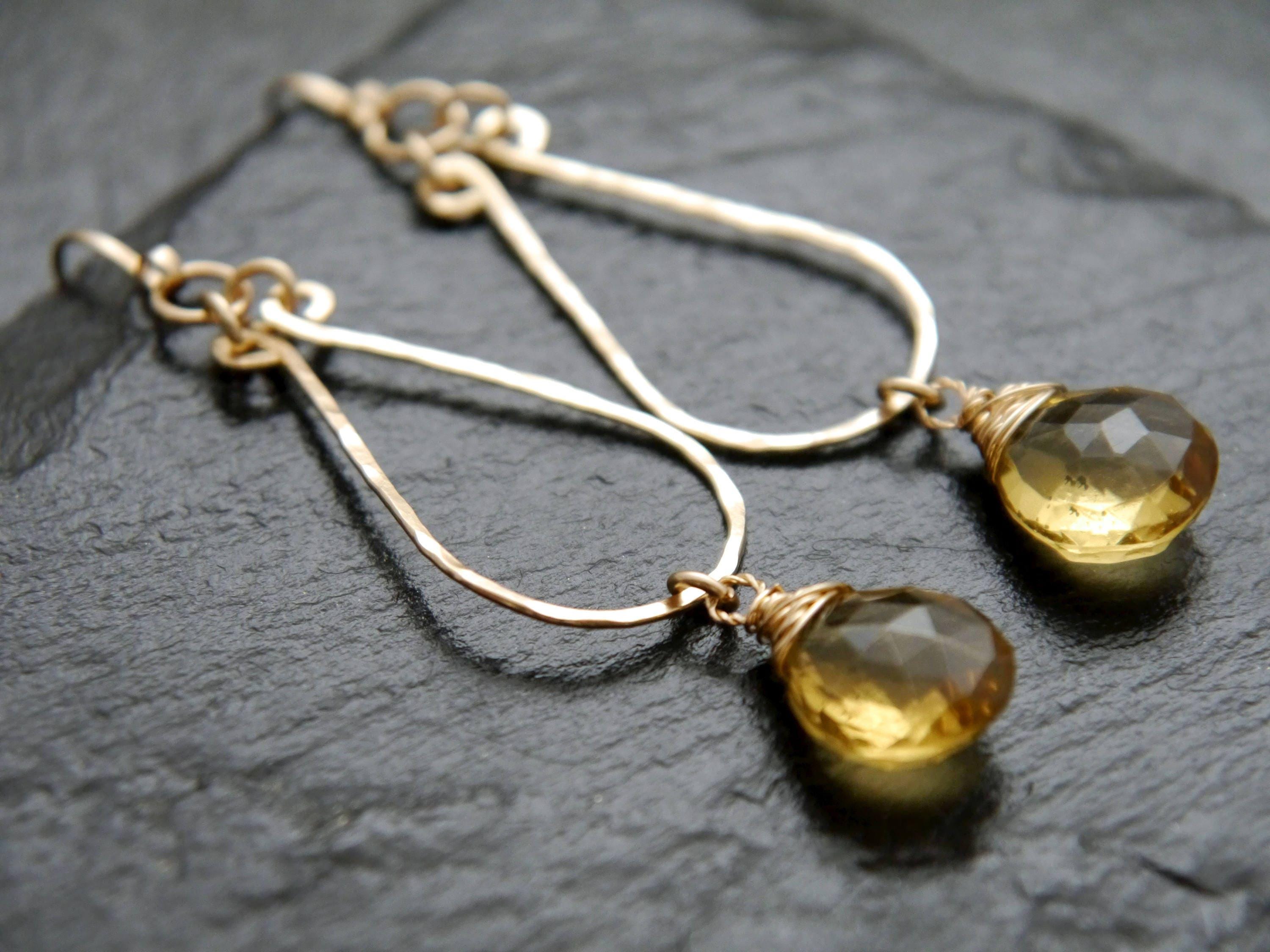 A pair of gold earrings with yellow gemstone pendants, resting on a dark surface.