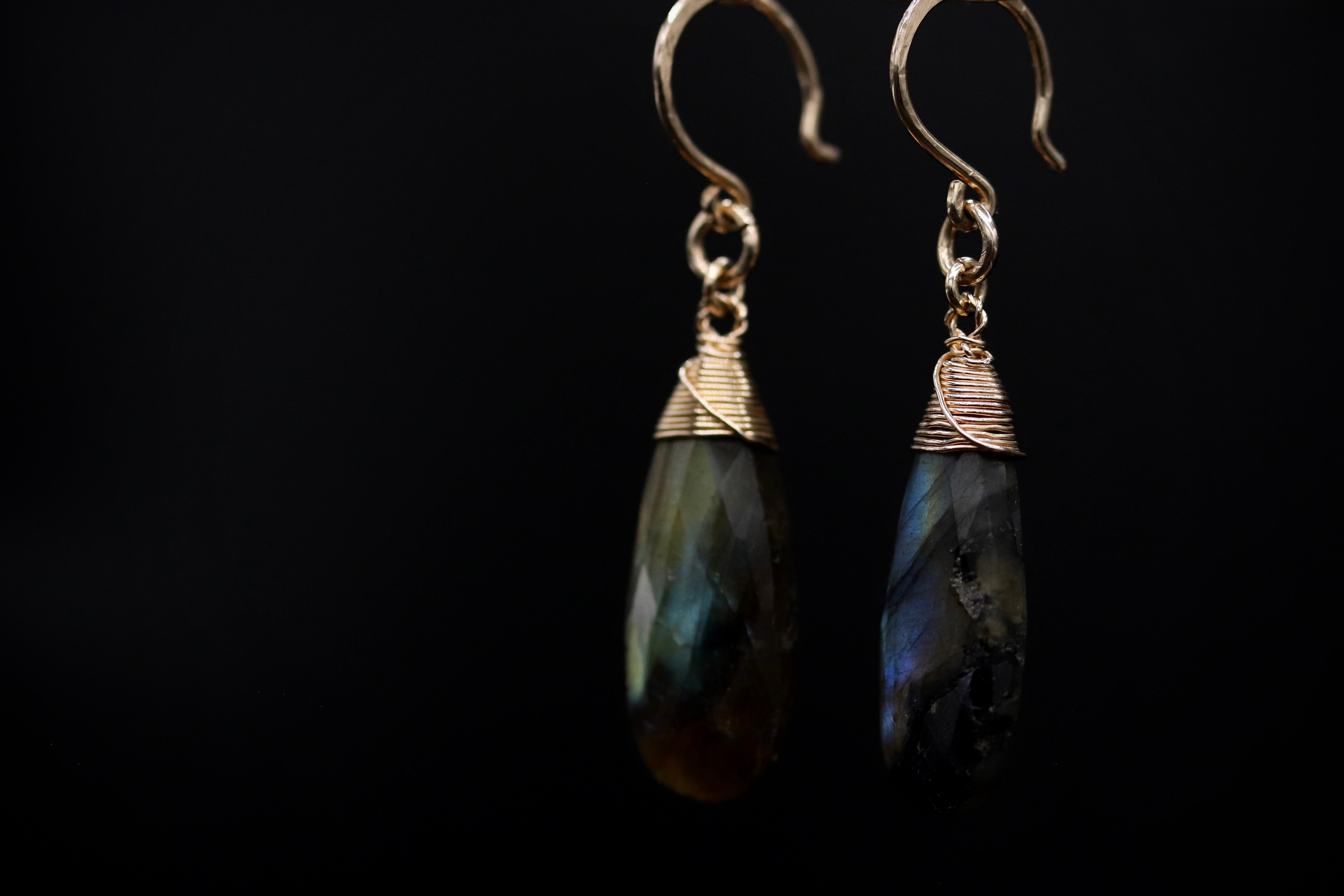 A pair of elegant earrings with a dark stone pendant and a gold-colored metal hook.