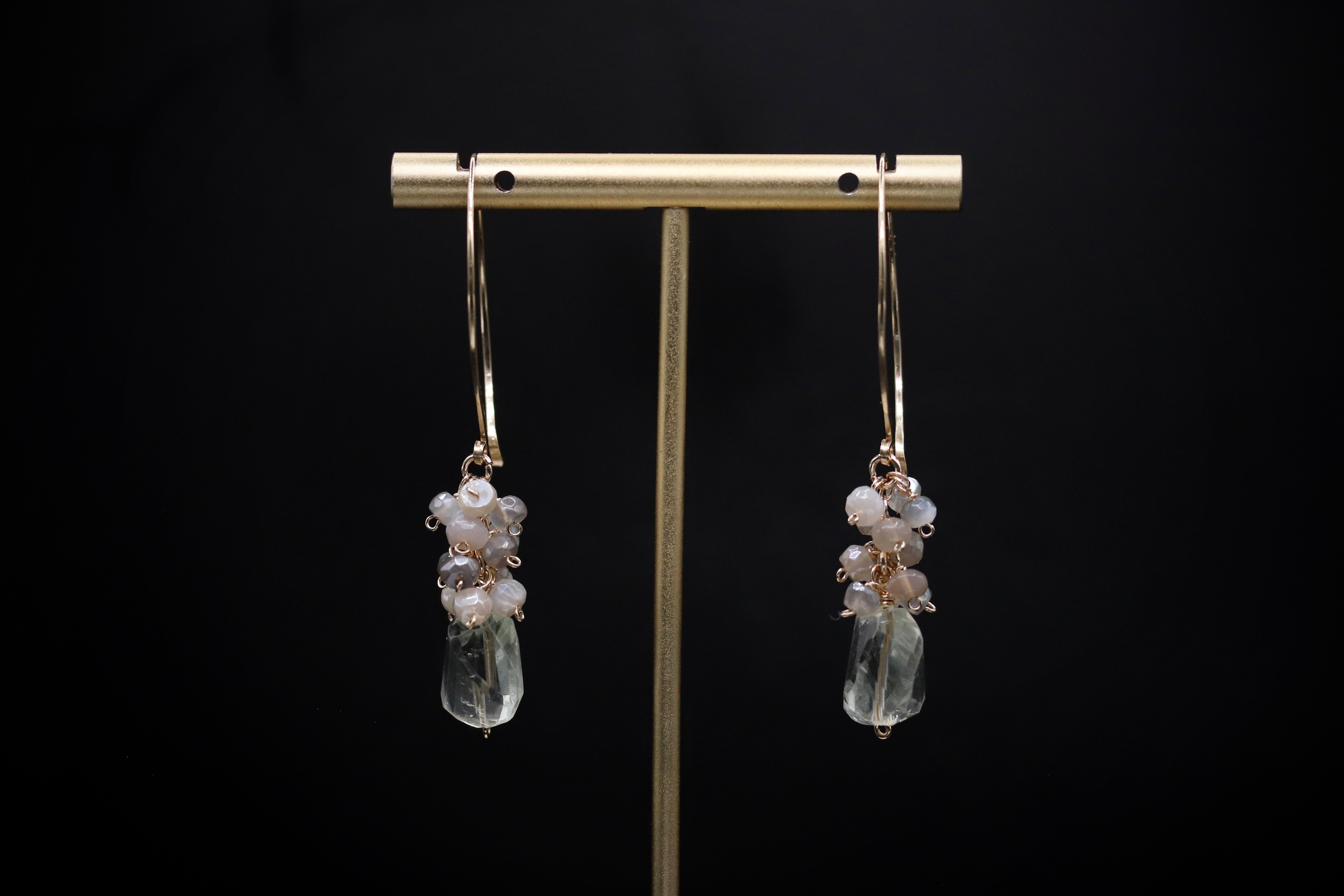 A pair of elegant earrings with clear gemstone accents hanging from a gold-colored metal stand against a black background.