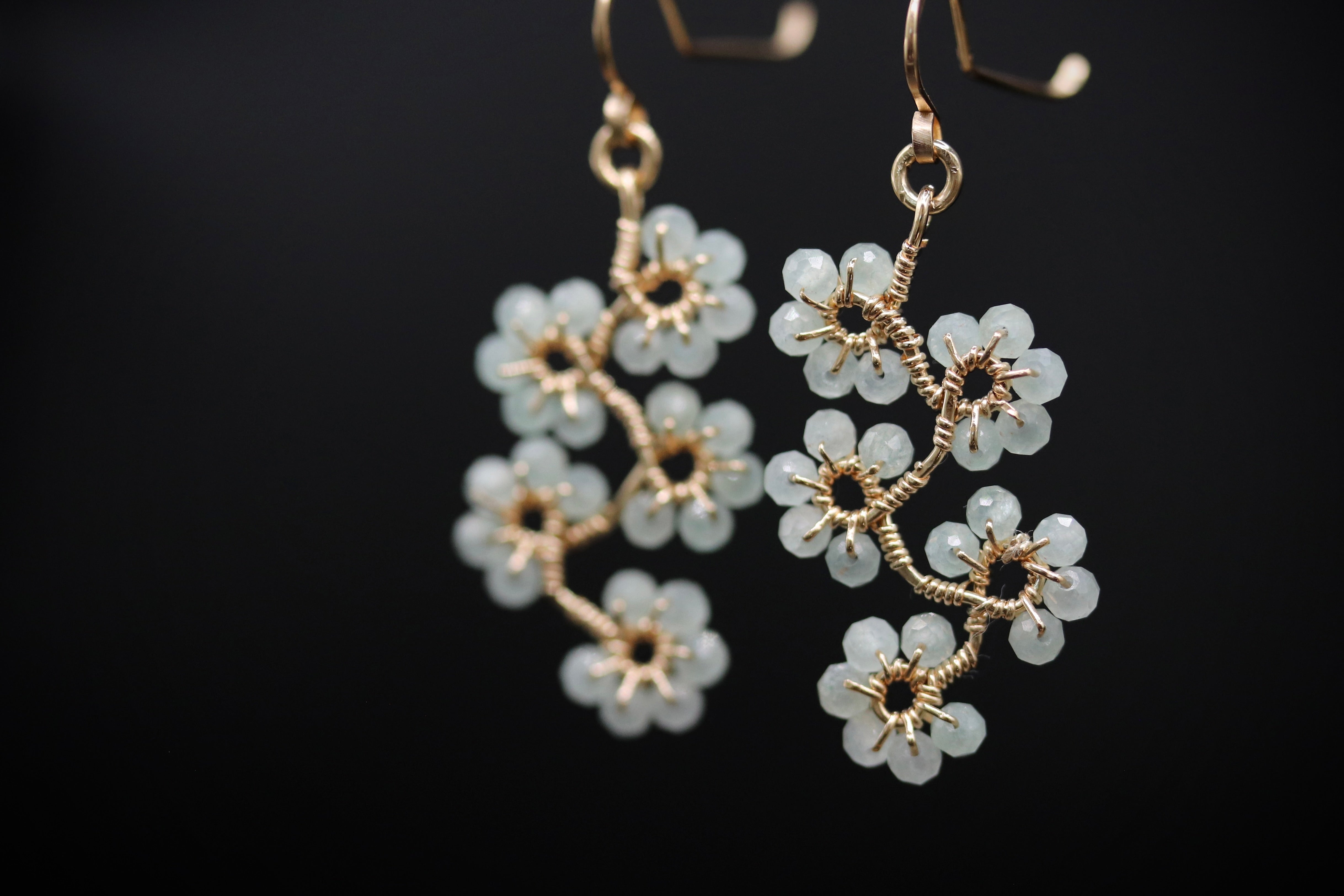 A pair of delicate earrings with white flower-shaped charms made of small, clear beads attached to a gold-colored metal frame.
