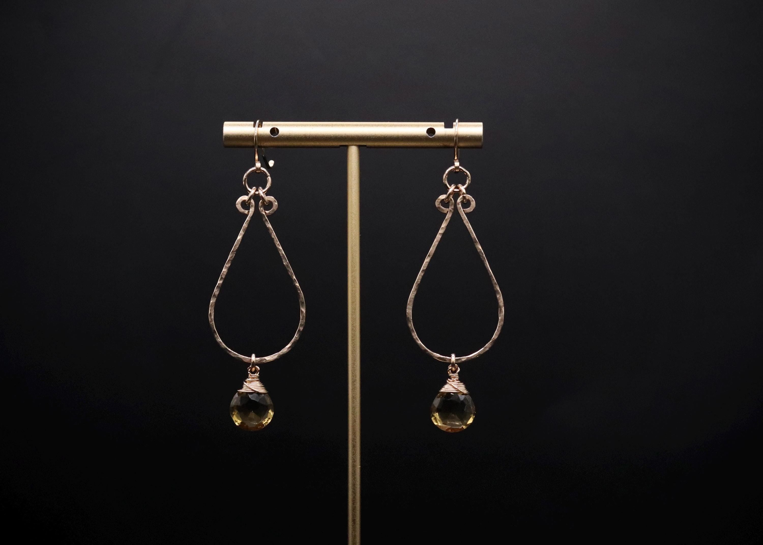 A pair of gold earrings with green gemstones hanging from the ear hooks, displayed on a gold stand against a black background.