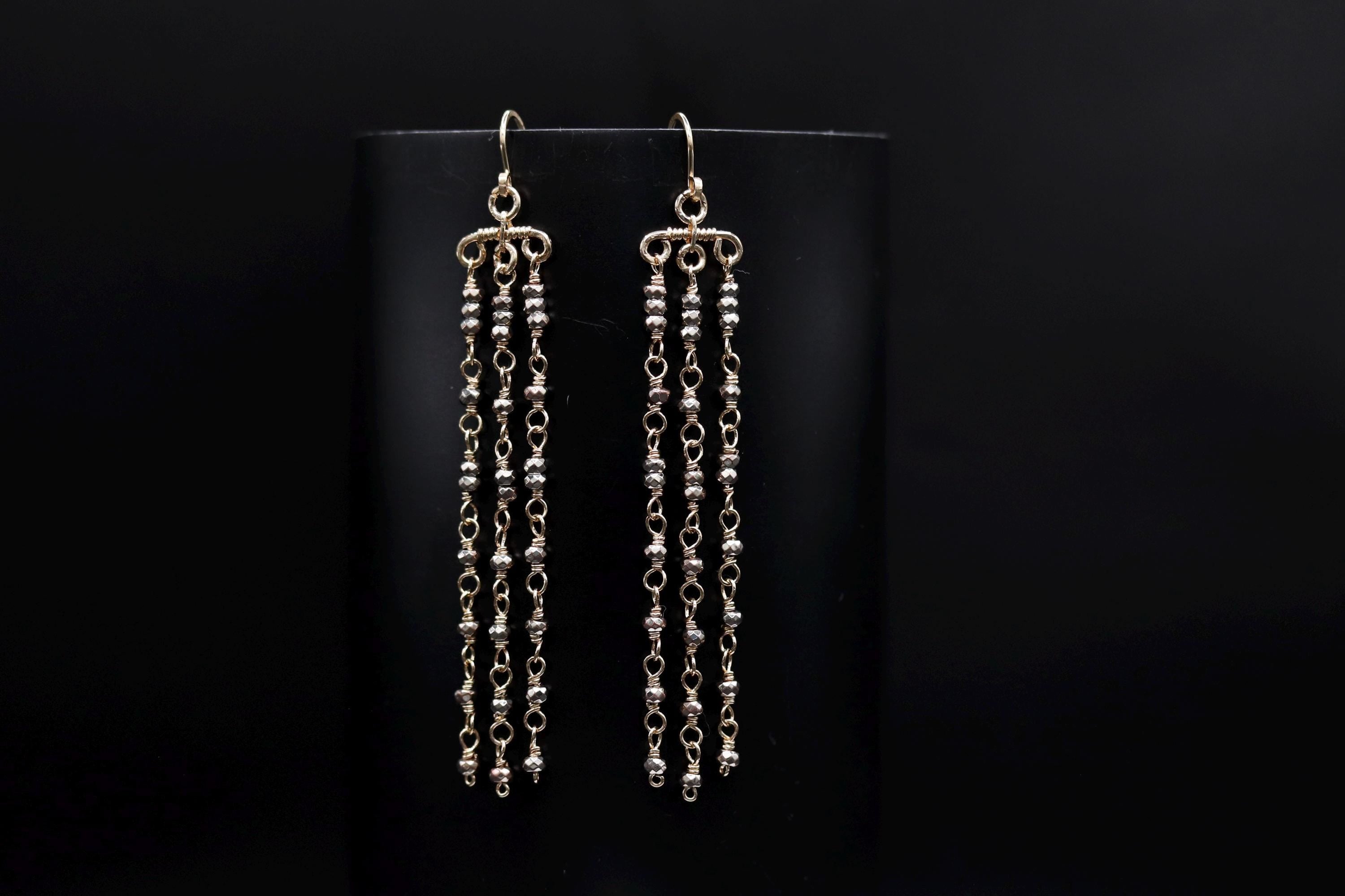 A pair of gold earrings with long, dangling chains against a black background.