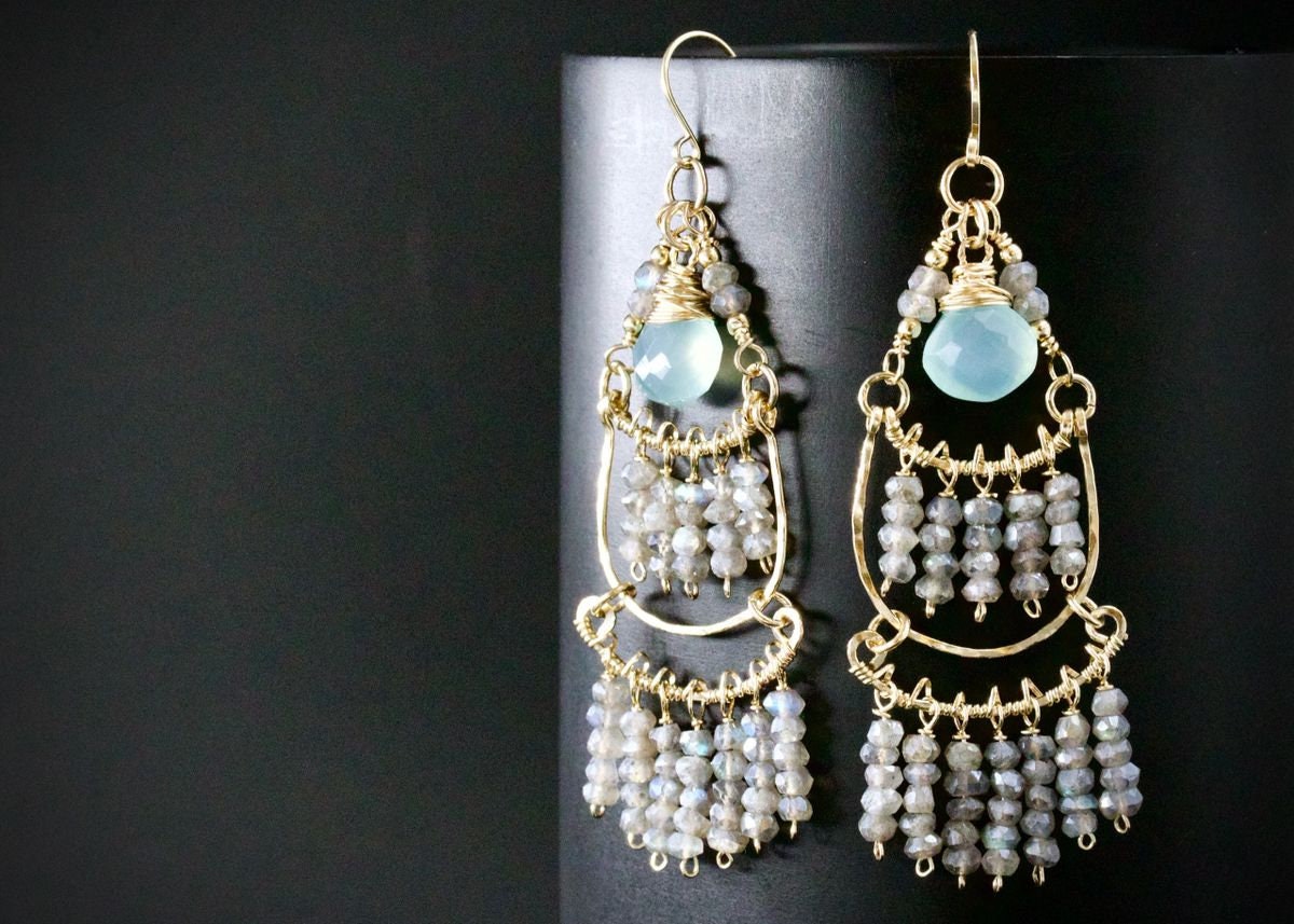 May include: Gold dangle earrings with a light blue gemstone and gray beads.
