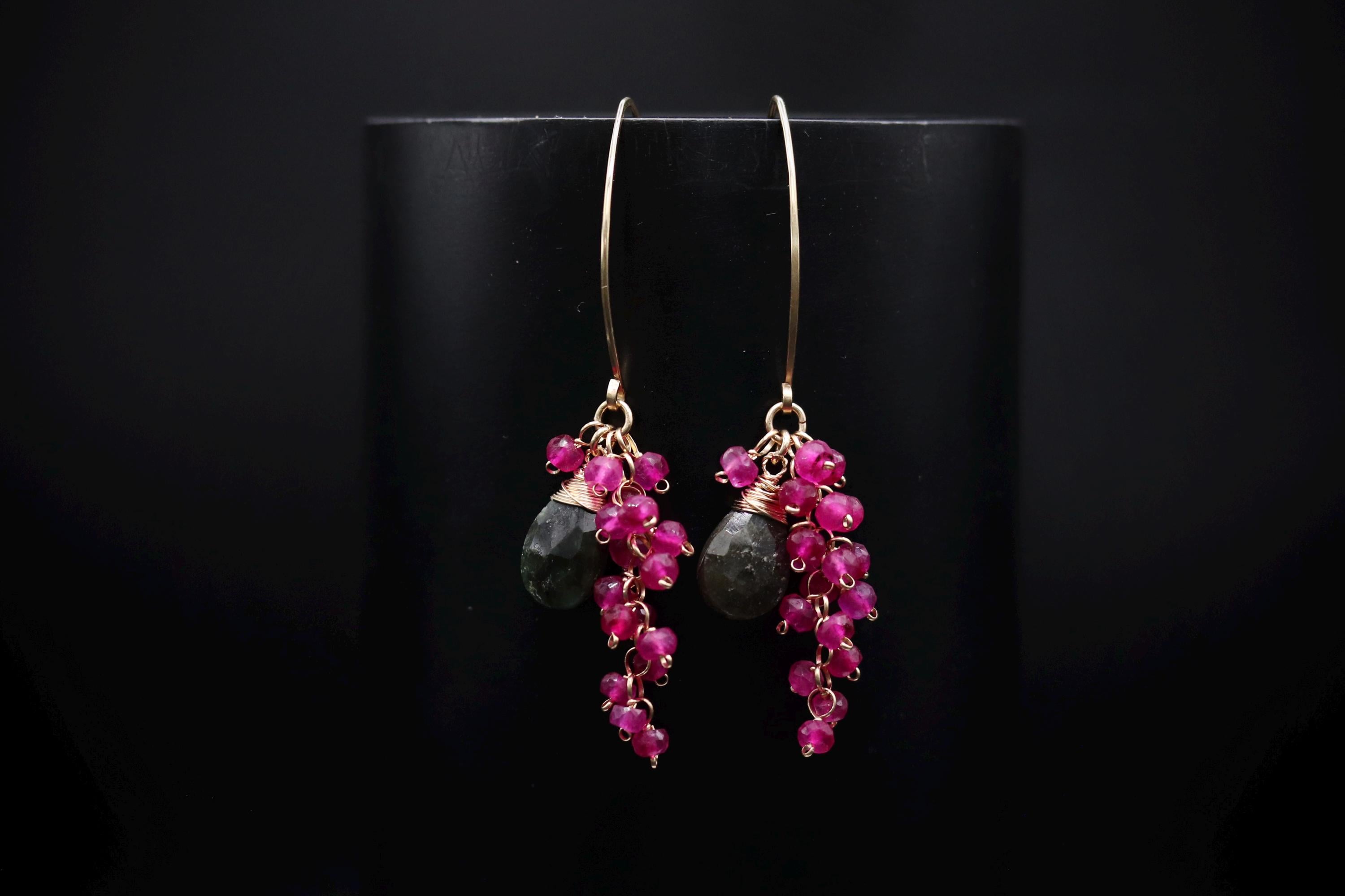 A pair of earrings with a black background and gold hooks, featuring a combination of red and green gemstones.