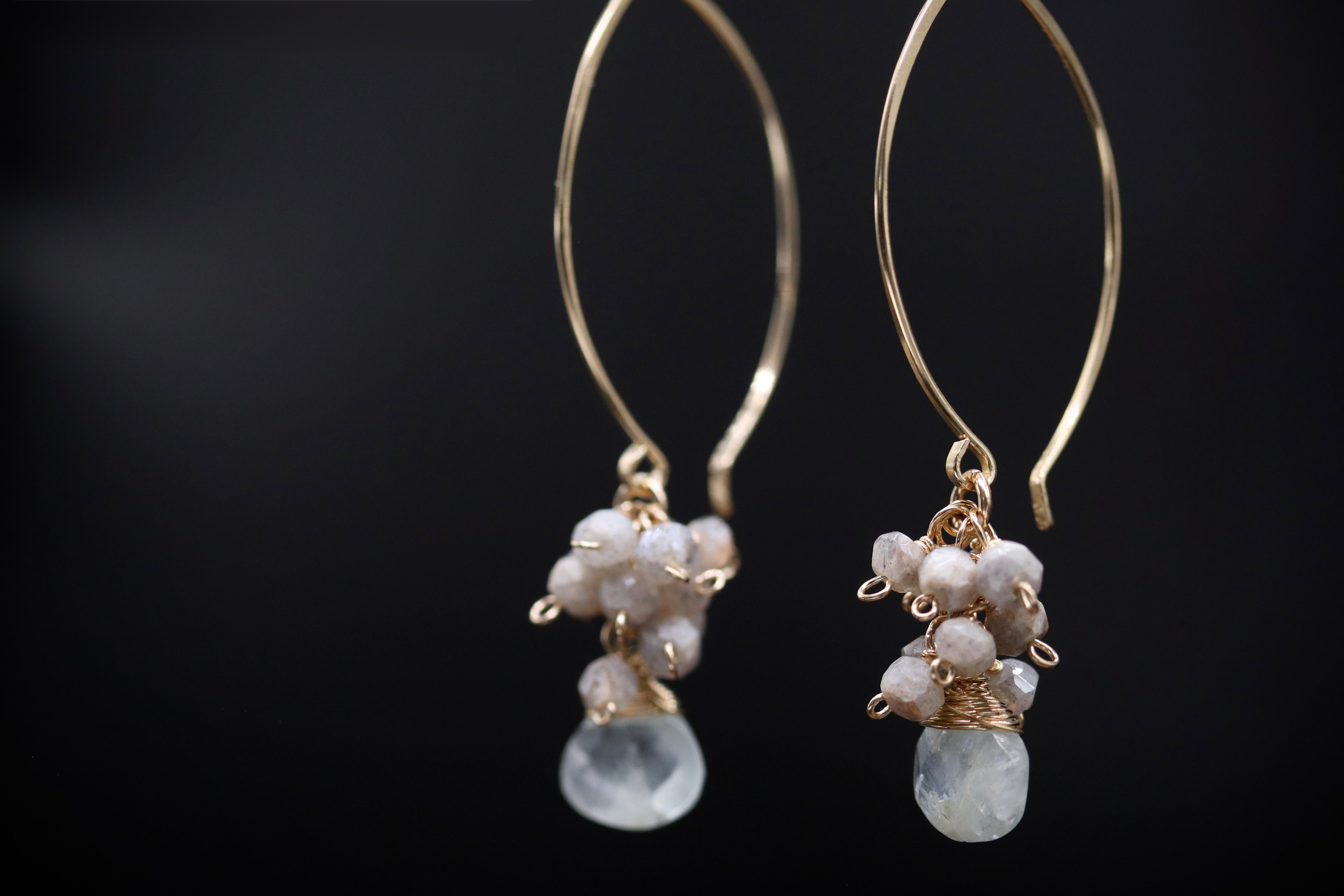 A pair of elegant gold earrings with white stones hanging from the bottom.