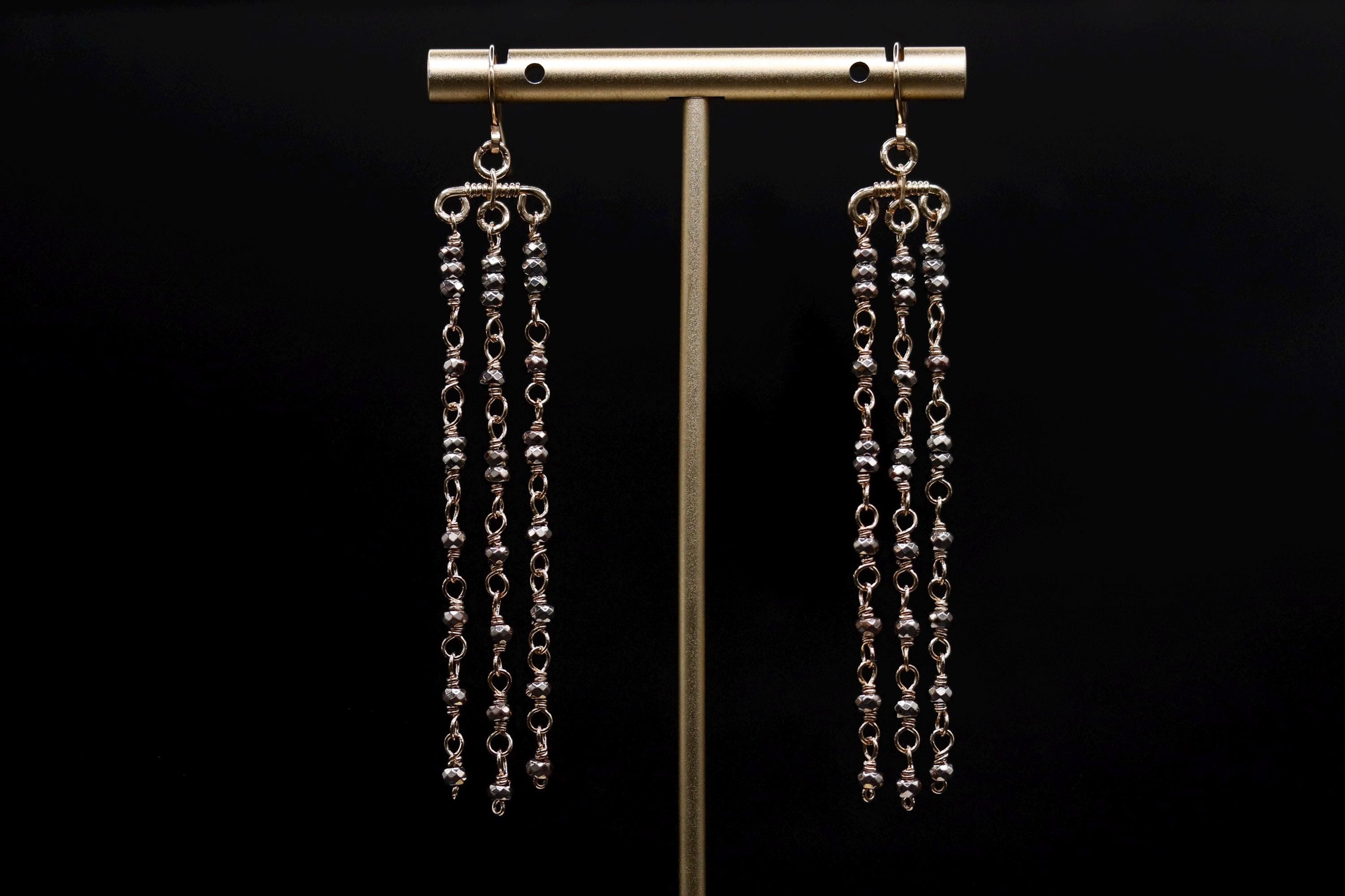 A pair of elegant gold earrings with long, dangling chains hanging from the ear hooks against a black background.