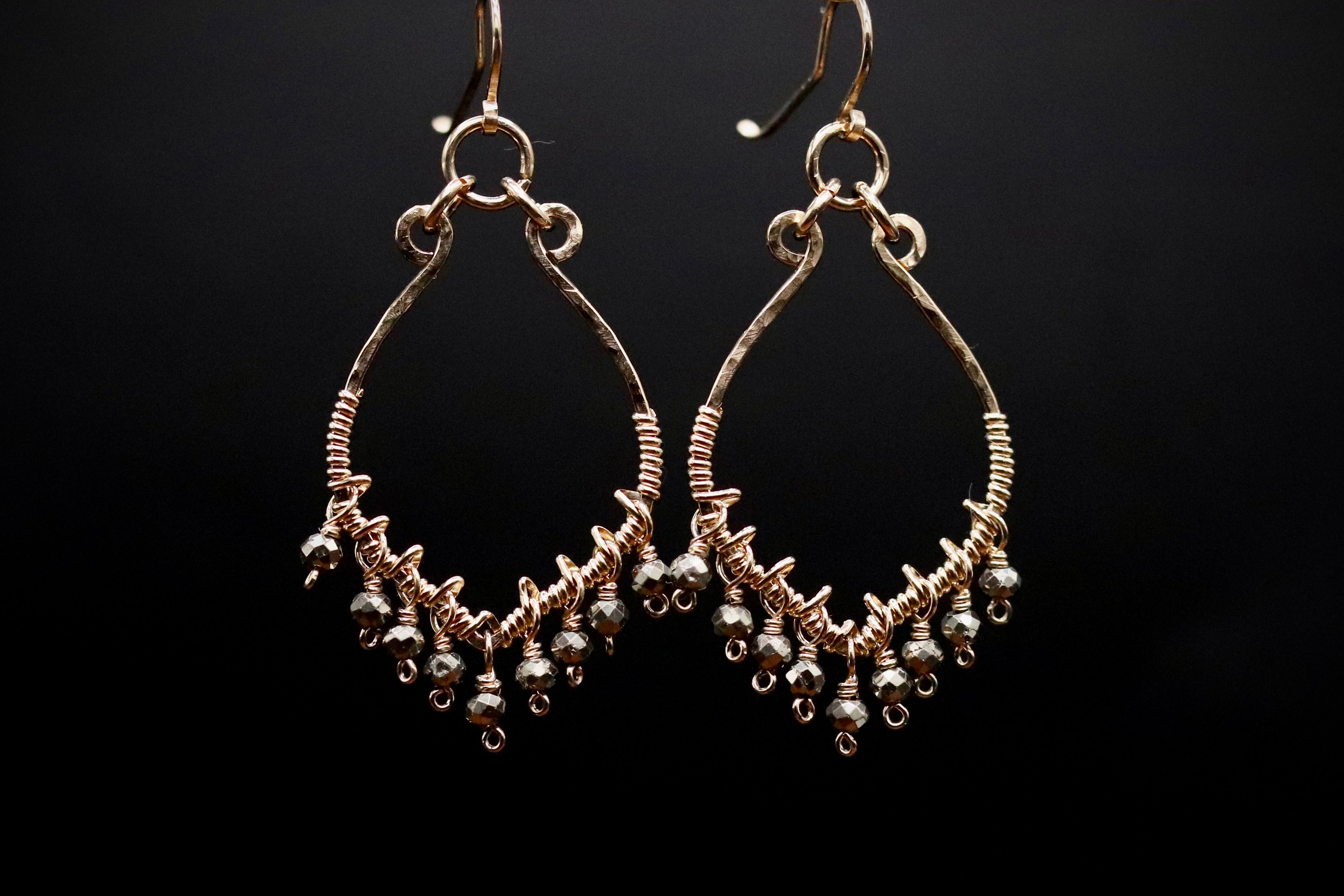 A pair of gold earrings with dangling beads and a metallic design against a black background.