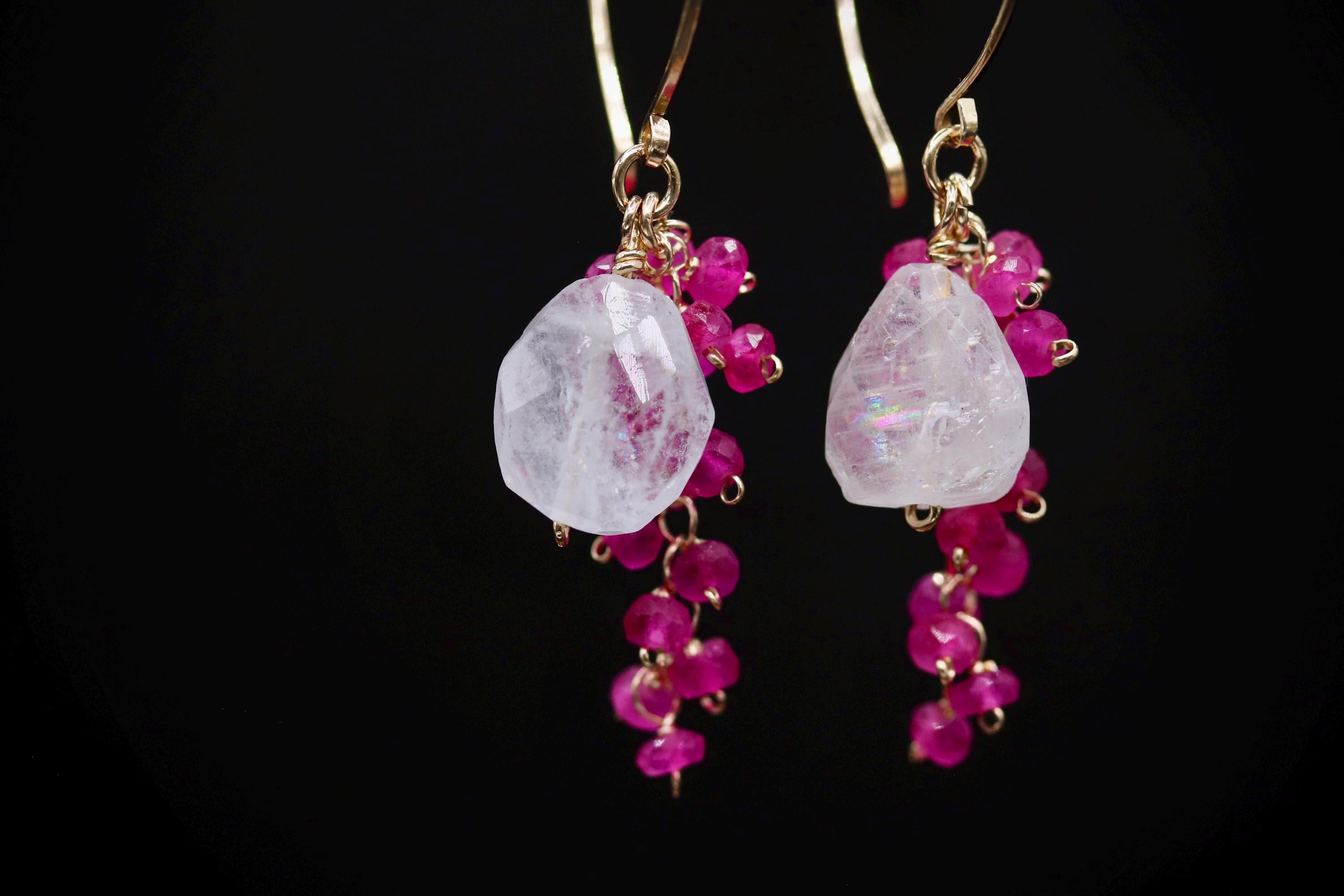 A pair of elegant earrings with a combination of white and pink gemstones, as well as small, dangling beads in a metallic color.