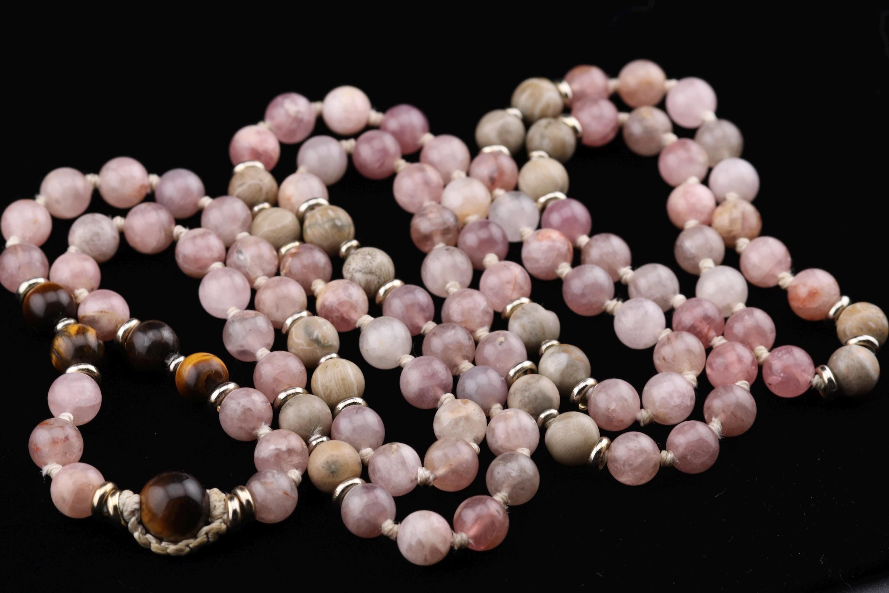 A necklace composed of numerous small beads in various shades of pink and gray, arranged in a decorative pattern.