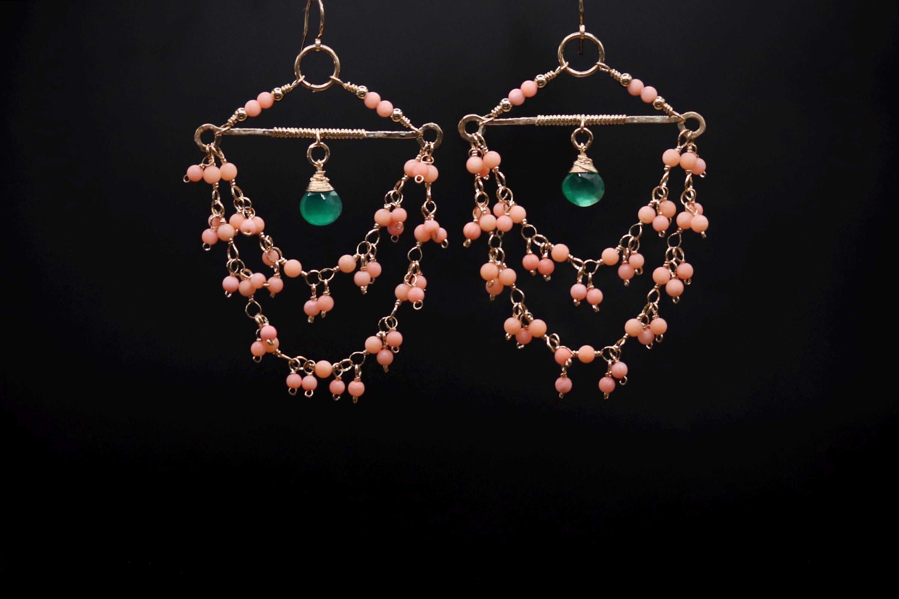 A pair of earrings with a green gemstone and pink beads hanging from a wire frame.