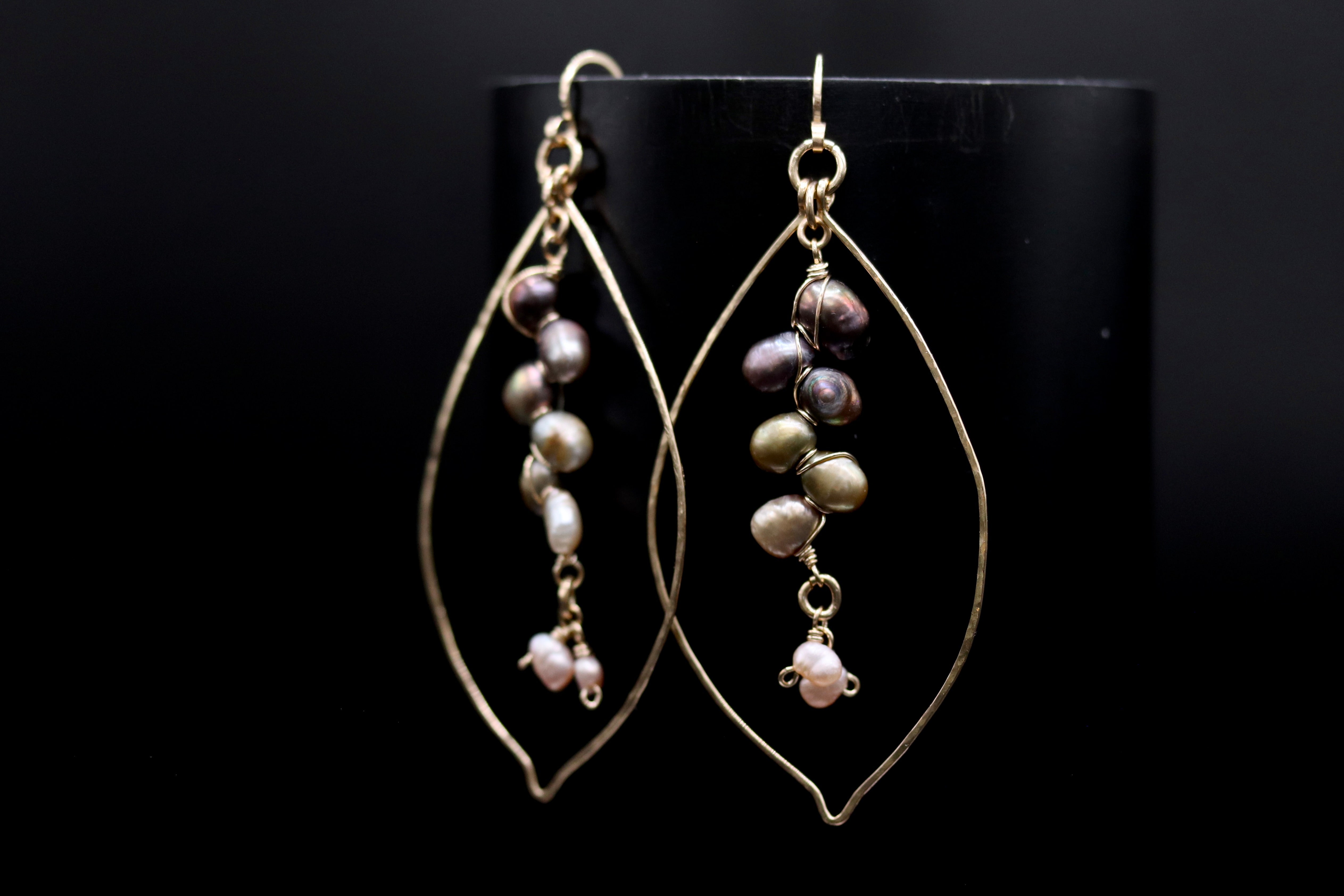 A pair of gold earrings with a leaf-shaped design, featuring multiple pearls hanging from the center.
