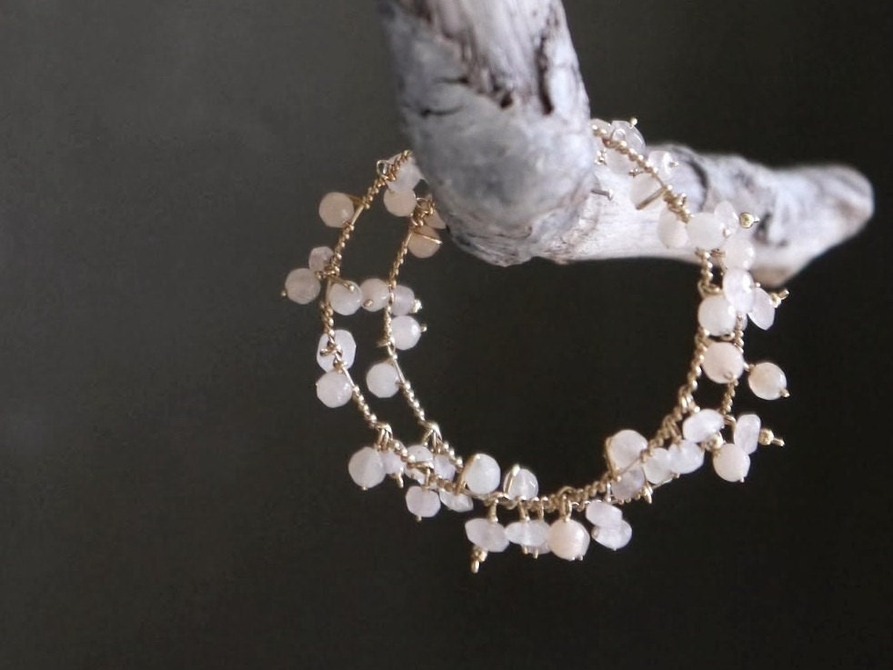 May include: A delicate gold hoop earring with a cluster of small, pale pink stones dangling from it.