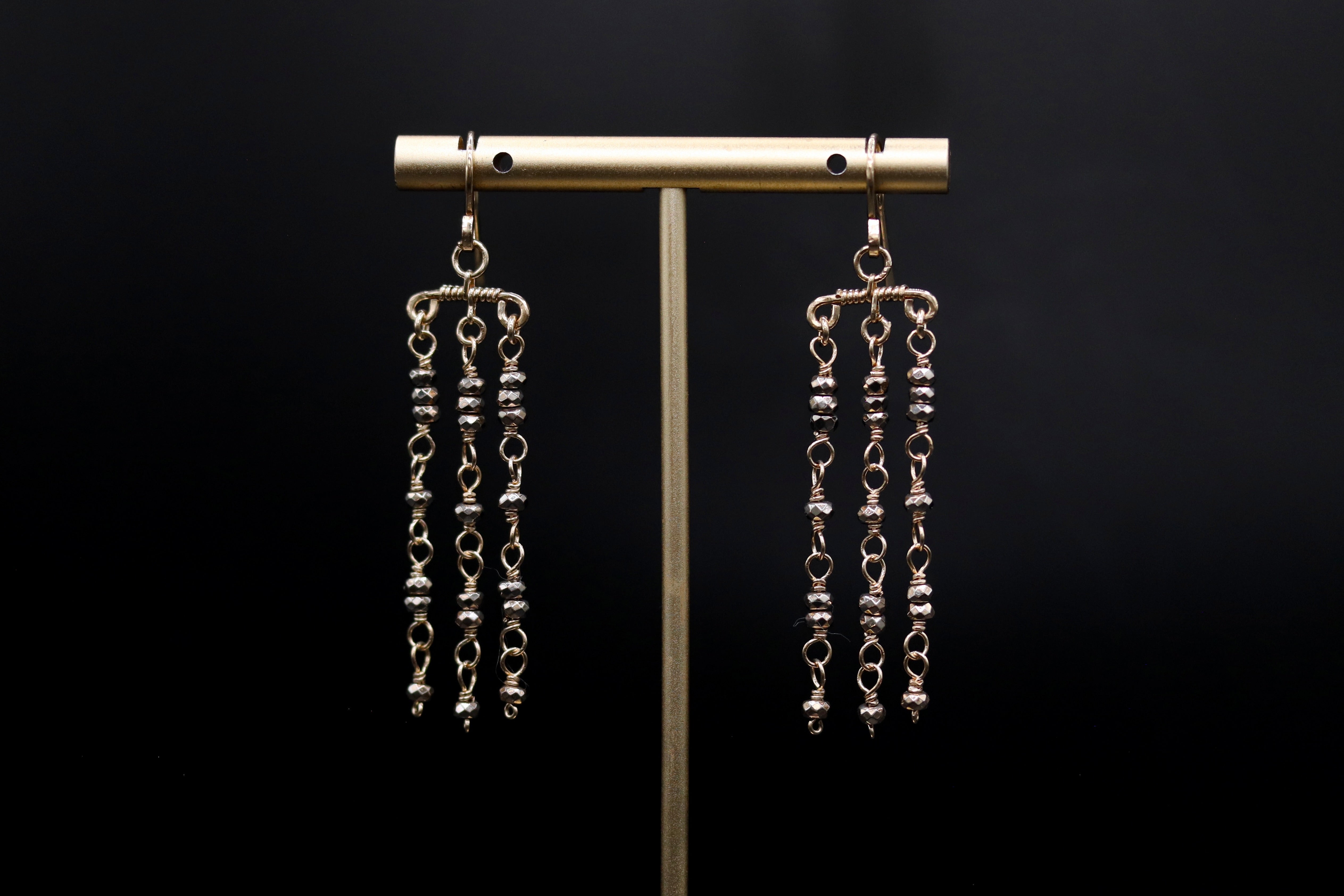 A pair of elegant earrings with dangling metal chains and beads displayed on a stand against a dark background.