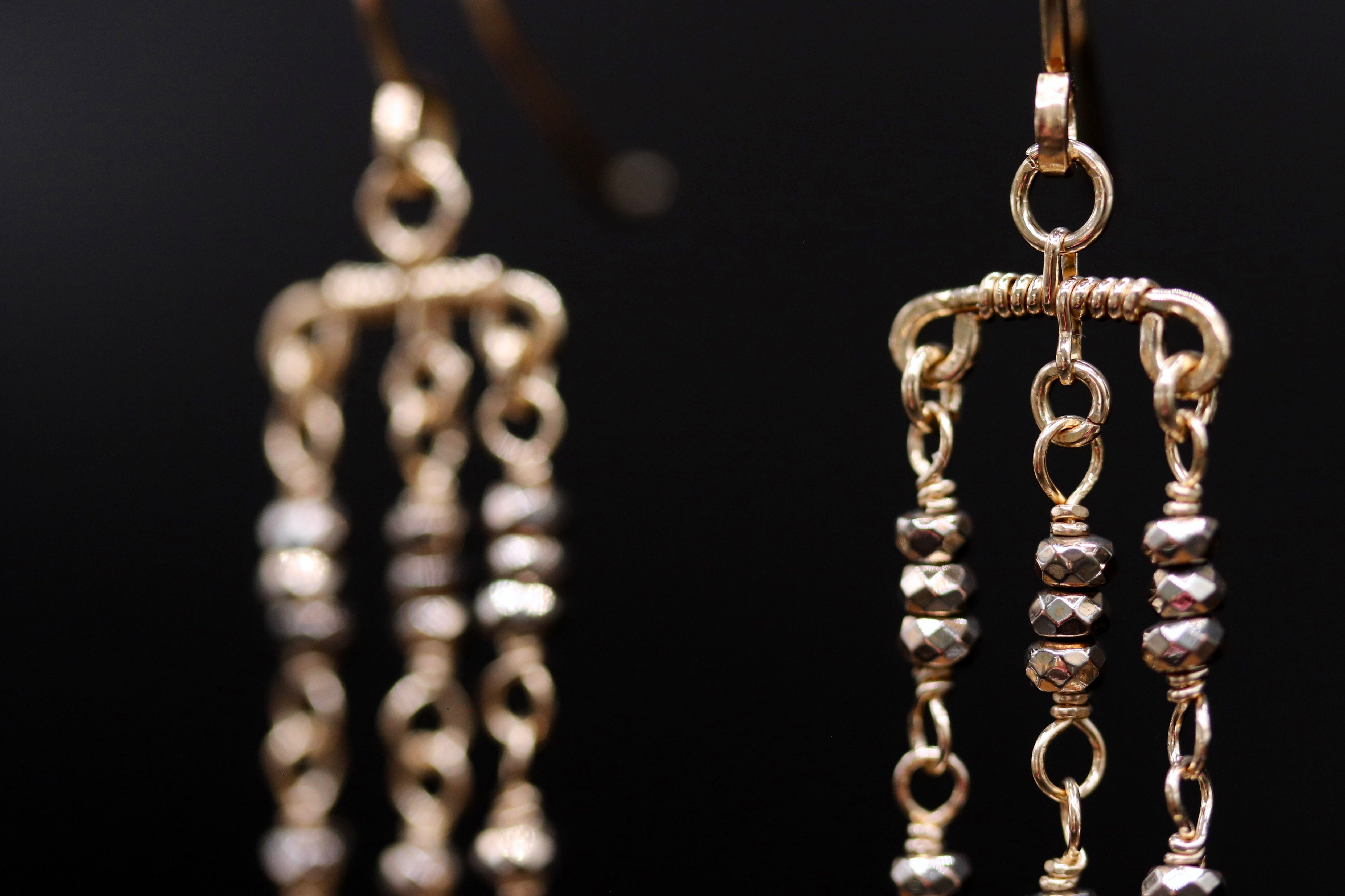A close-up view of a pair of gold earrings with multiple tiers of small, dangling beads.