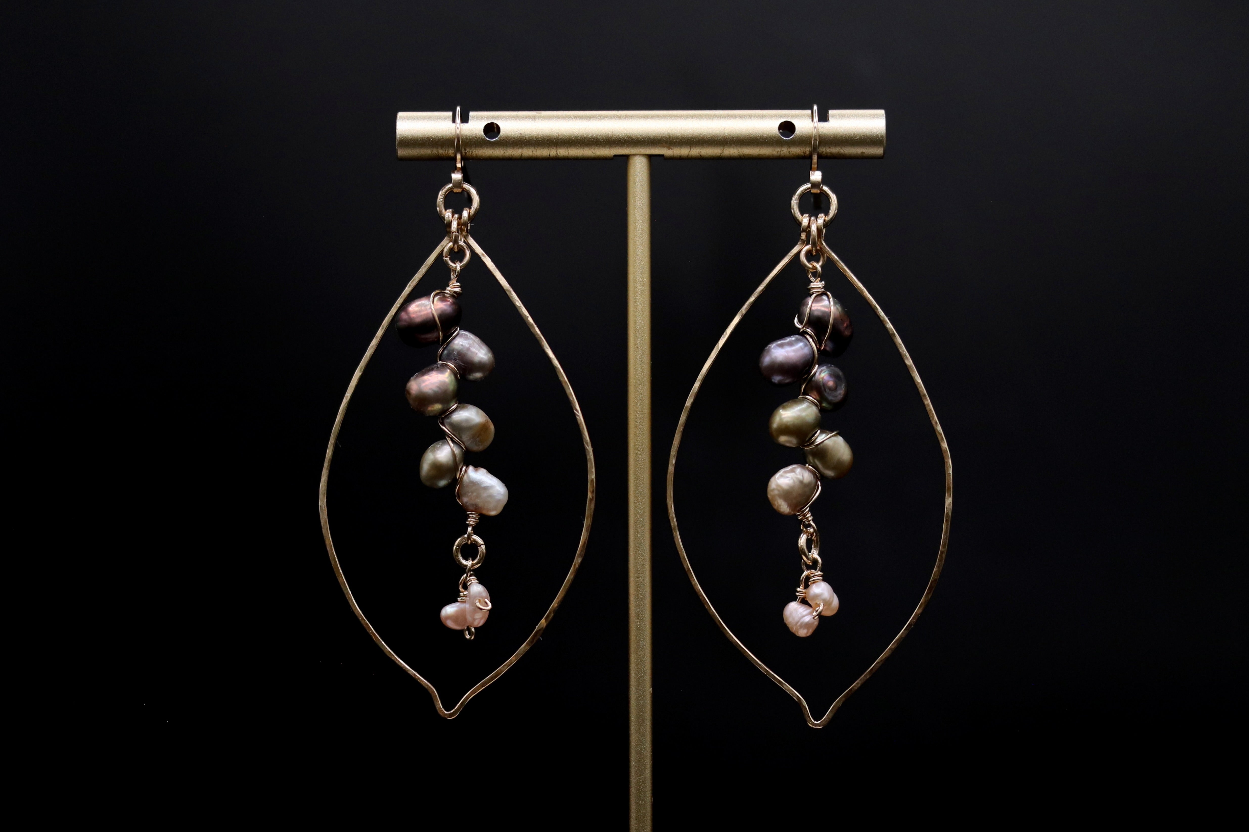 A pair of earrings with pearls hanging from a gold-colored metal frame against a black background.