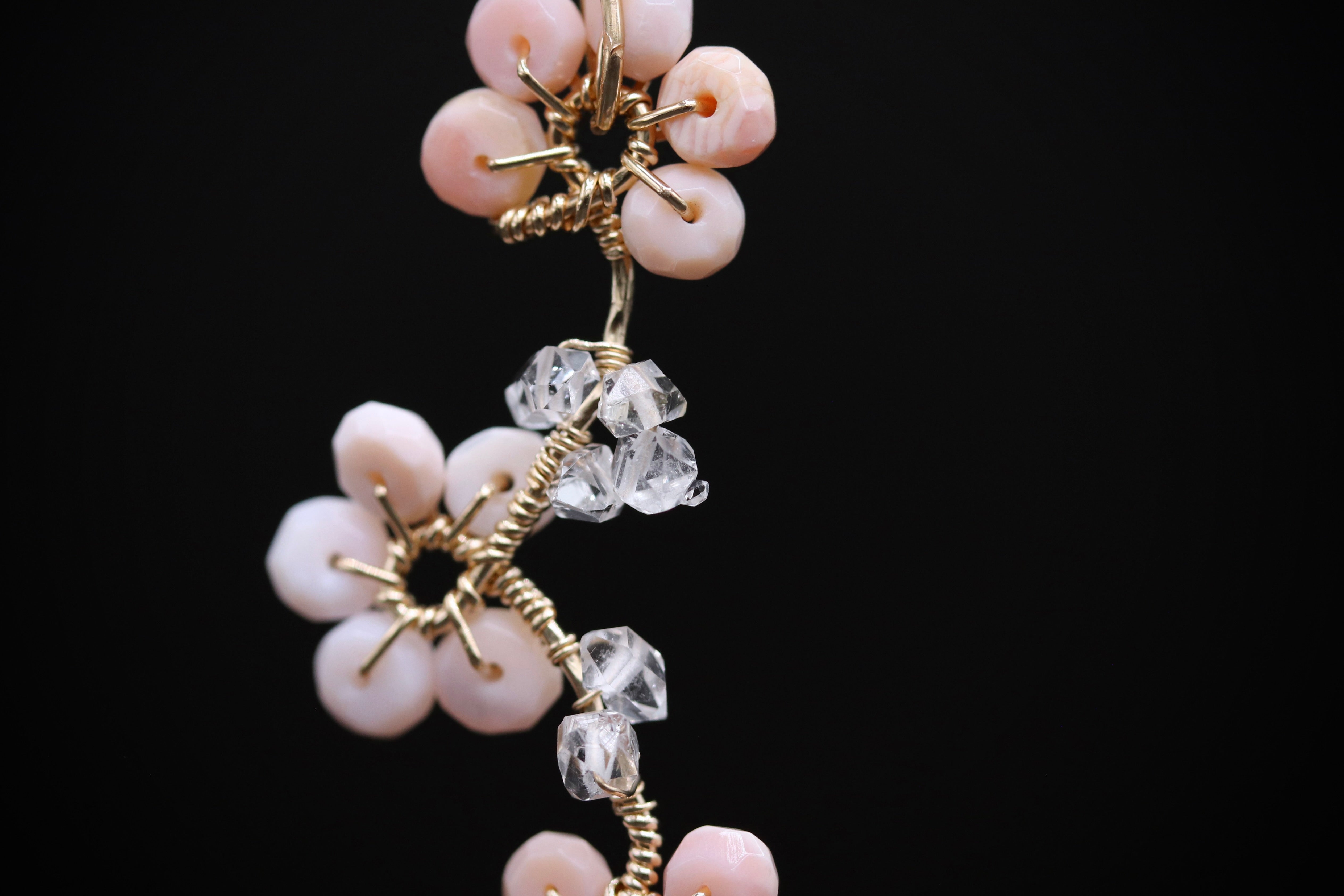 A close-up view of a delicate necklace with a floral design, featuring small pink beads and clear crystal accents.