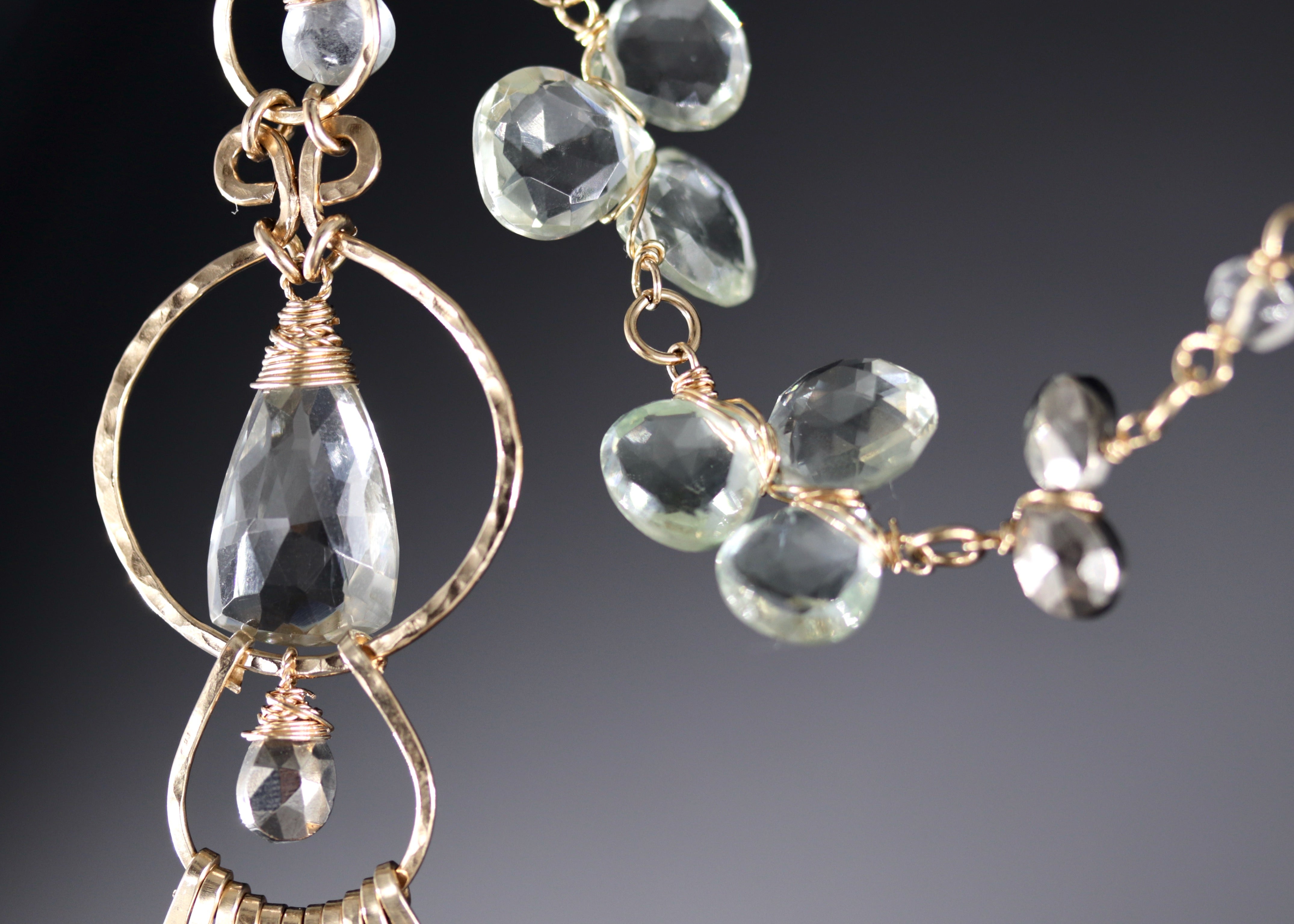 a close-up view of a pair of elegant necklaces with clear gemstones. The necklace on the left has a large crystal pendant, while the necklace on the right has smaller crystal pendants. The necklaces are set against a dark background, which highlights their intricate designs and sparkling gemstones.