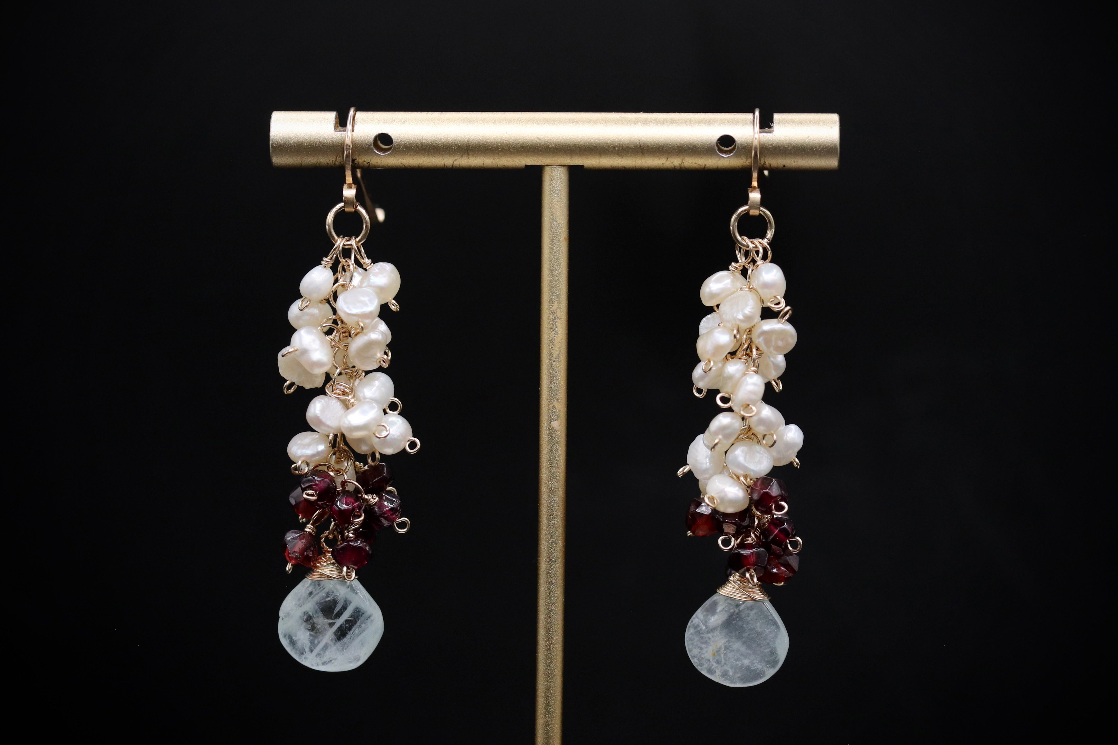 A pair of elegant earrings with white pearls and maroon gemstones hanging from the bottom.