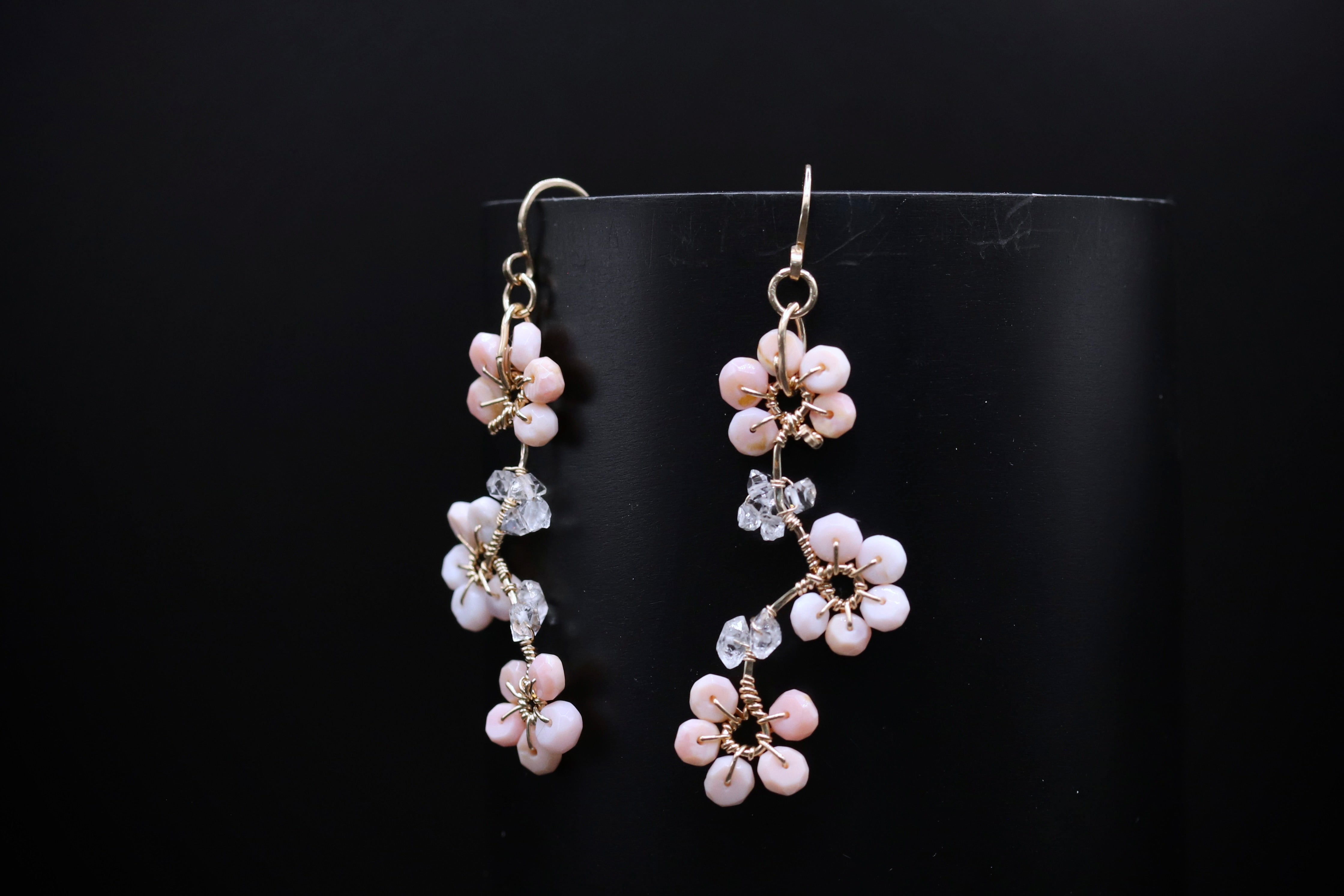 A pair of delicate earrings with small white flowers and clear gemstones, displayed against a black background.