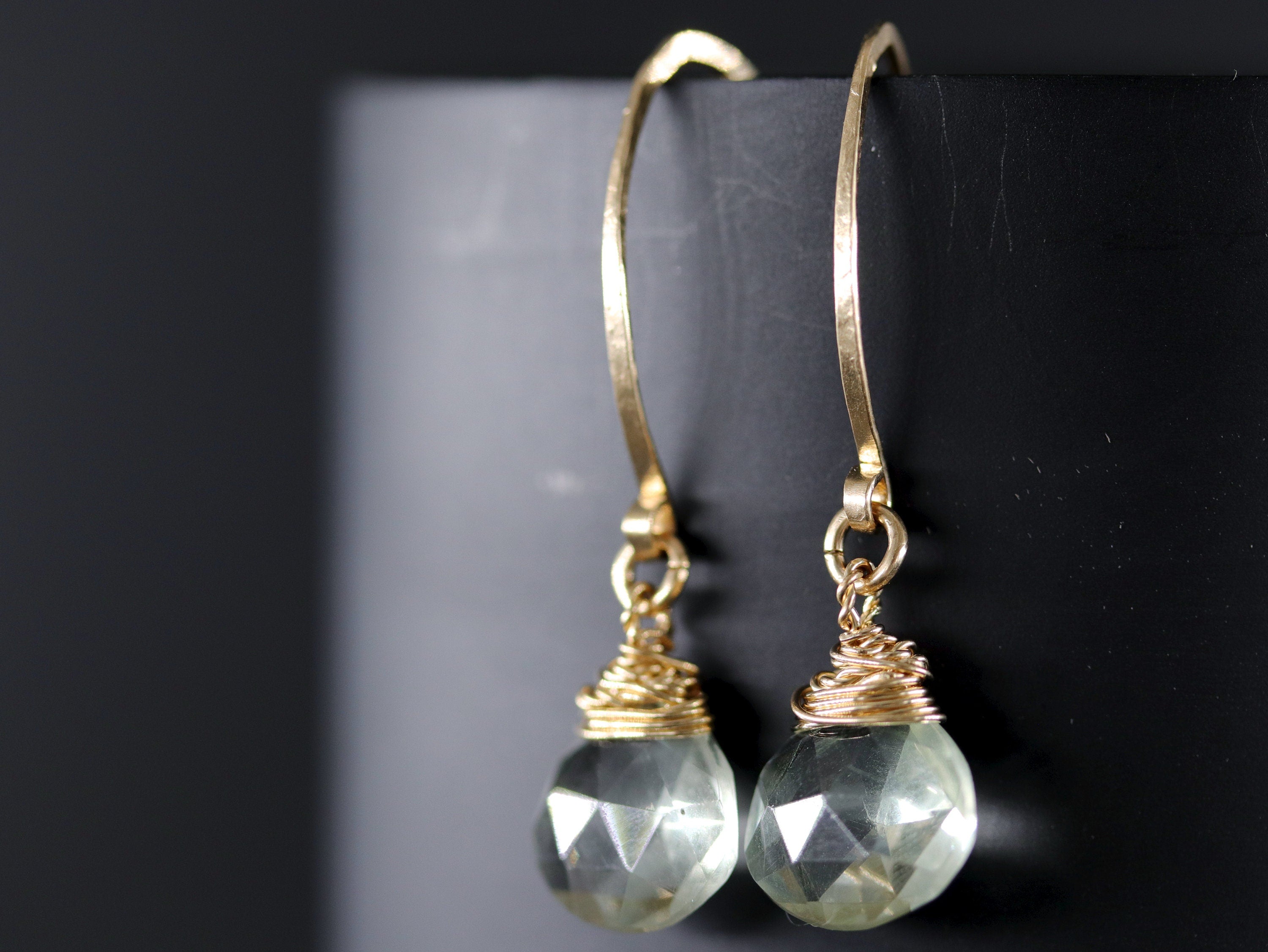 May include: A pair of gold earrings with green gemstone drops. The gemstones are faceted and wrapped in gold wire.