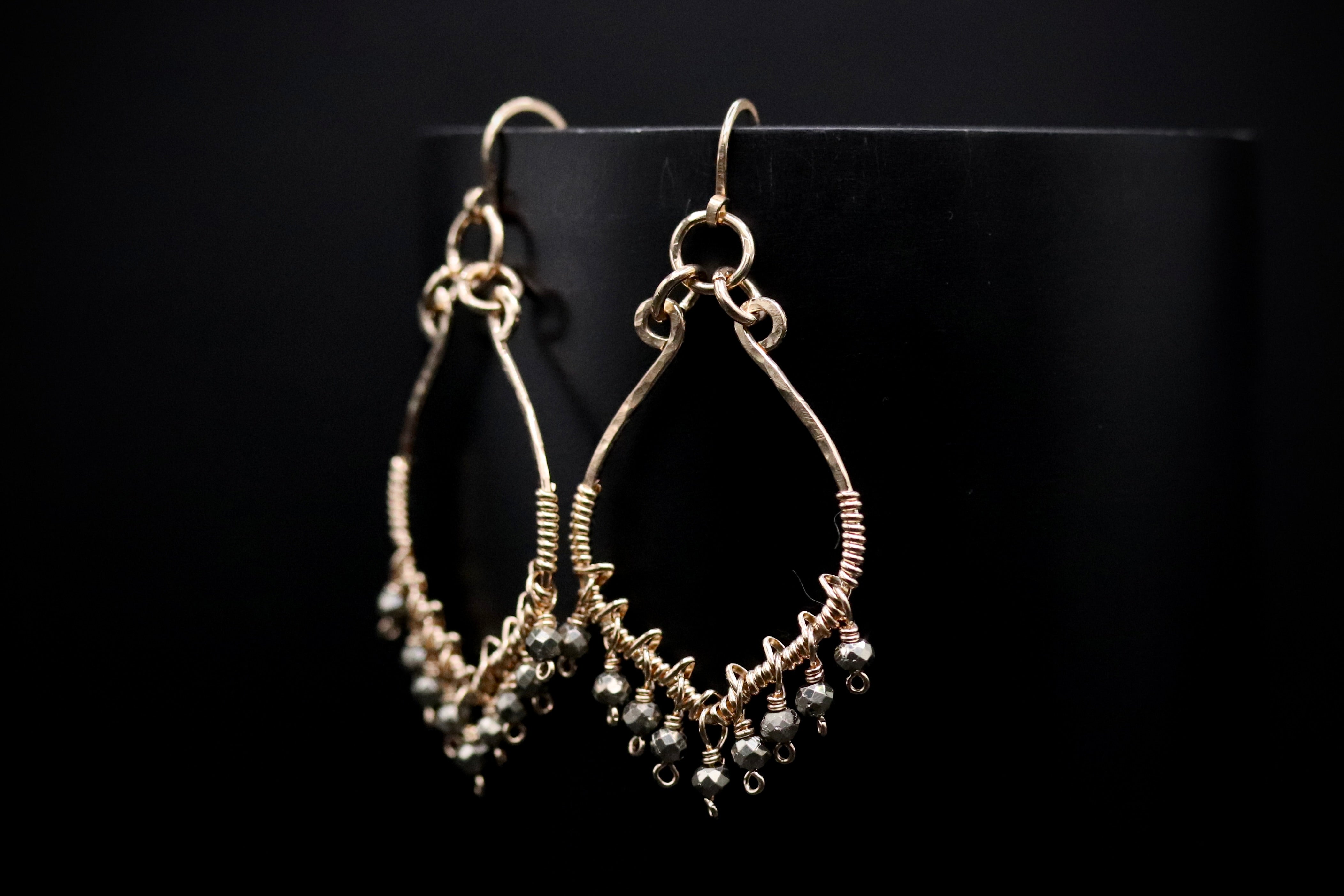 A pair of gold earrings with dangling beads, displayed against a black background.