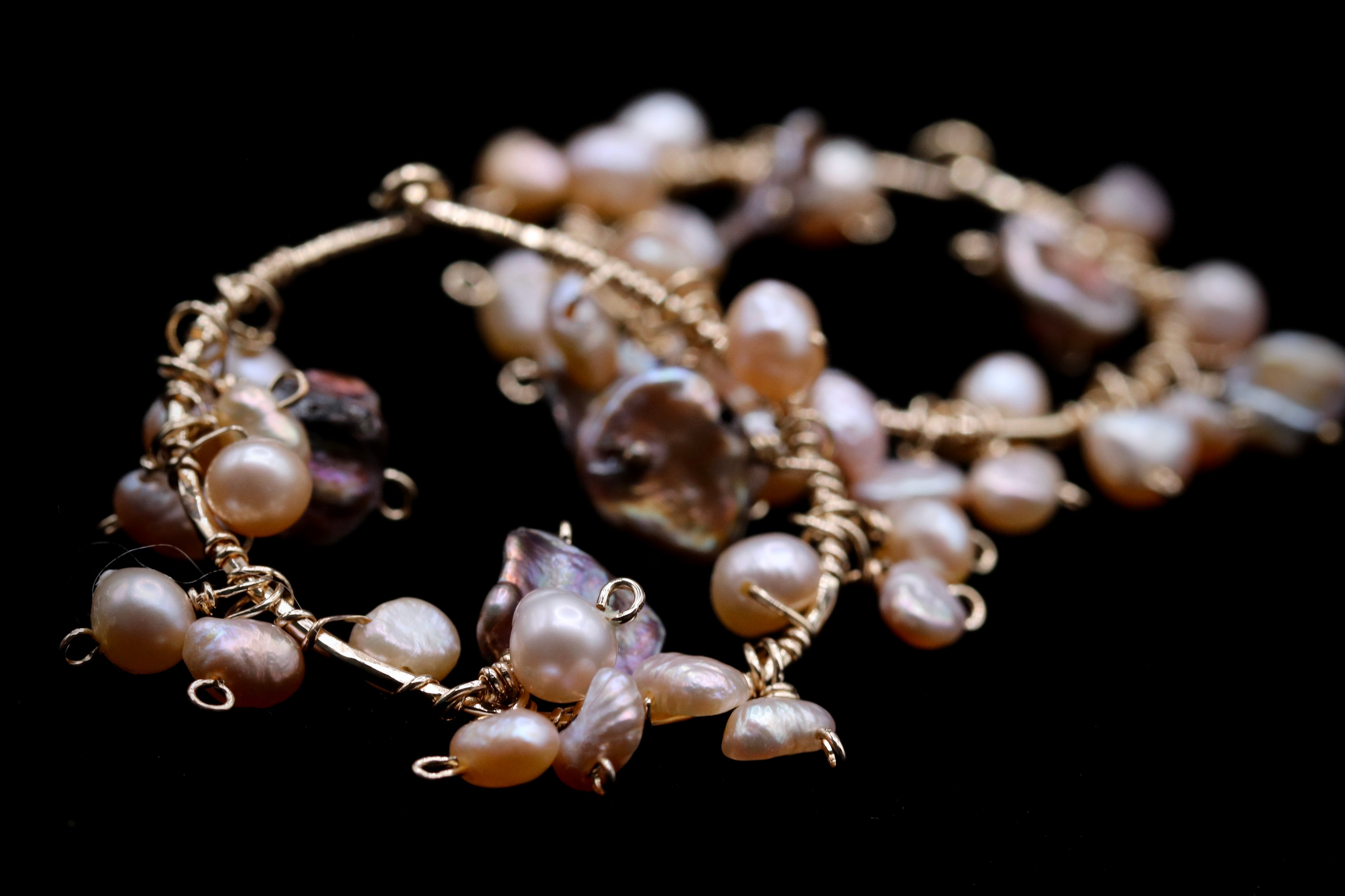 A close-up image of a delicate piece of jewelry, featuring a combination of pearls and wire elements.