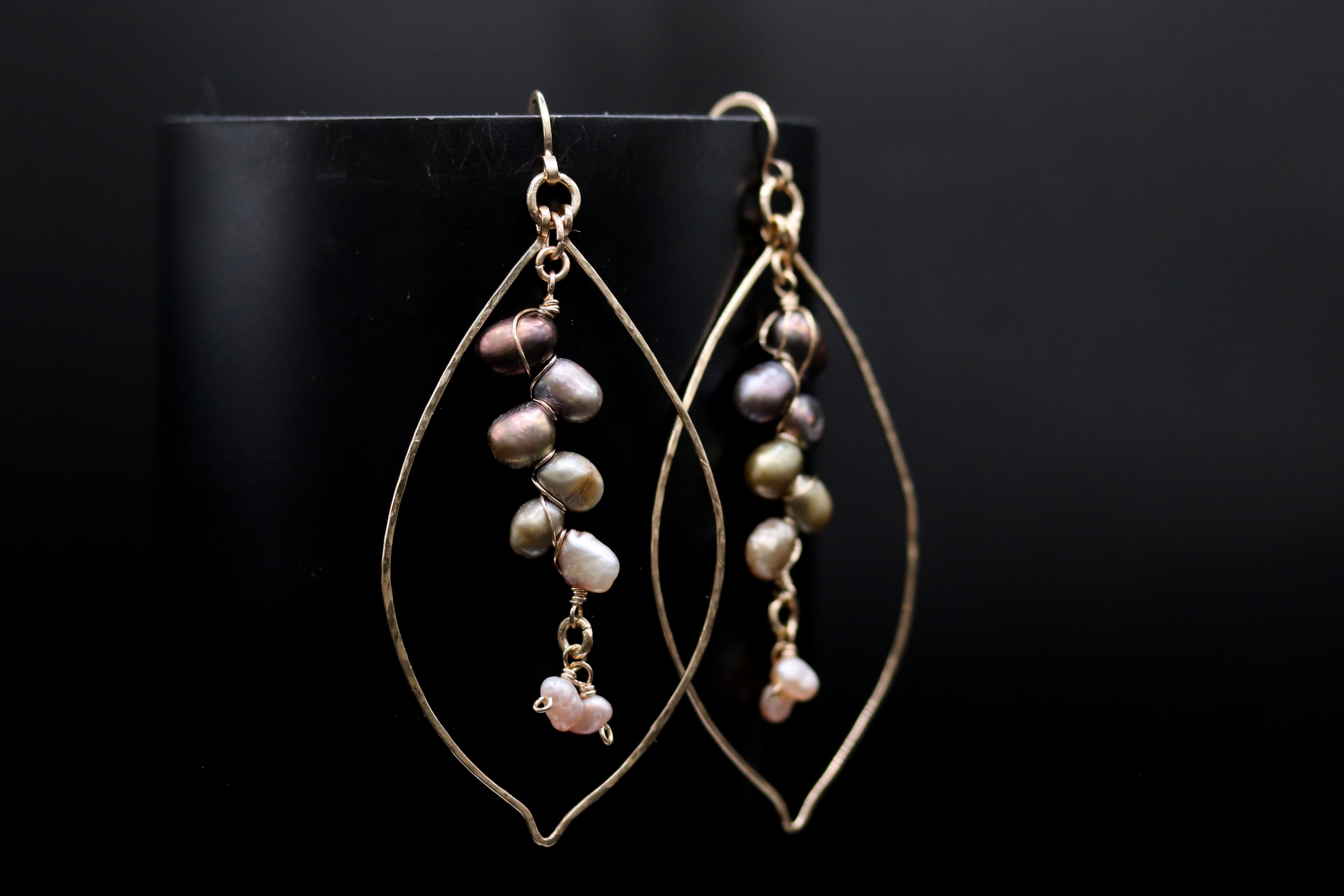 A pair of gold earrings with pearls hanging from the ends, displayed against a black background.