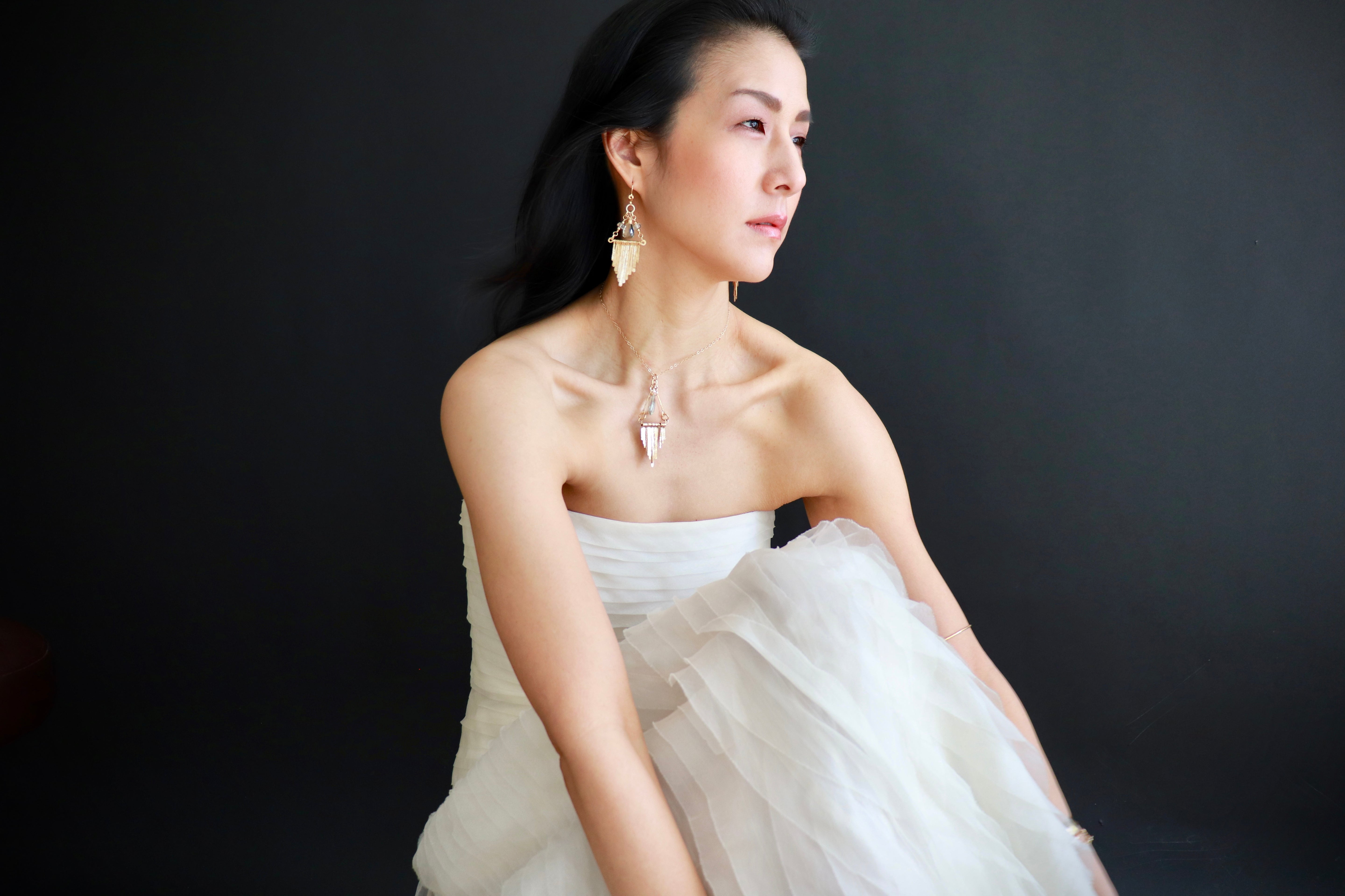 A woman in a white strapless dress poses against a dark background, her gaze directed off to the side.