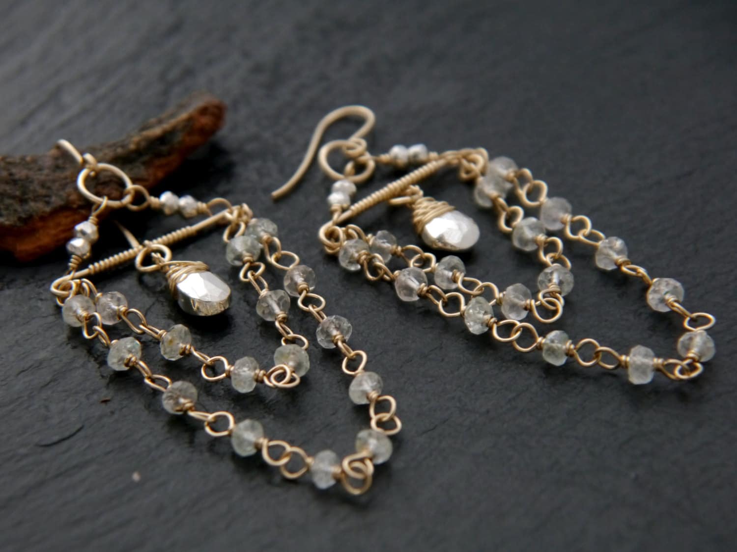 May include: A pair of gold-toned earrings with a delicate design. Each earring features a teardrop-shaped, faceted crystal pendant and strands of small, clear beads. The earrings have a hook closure.