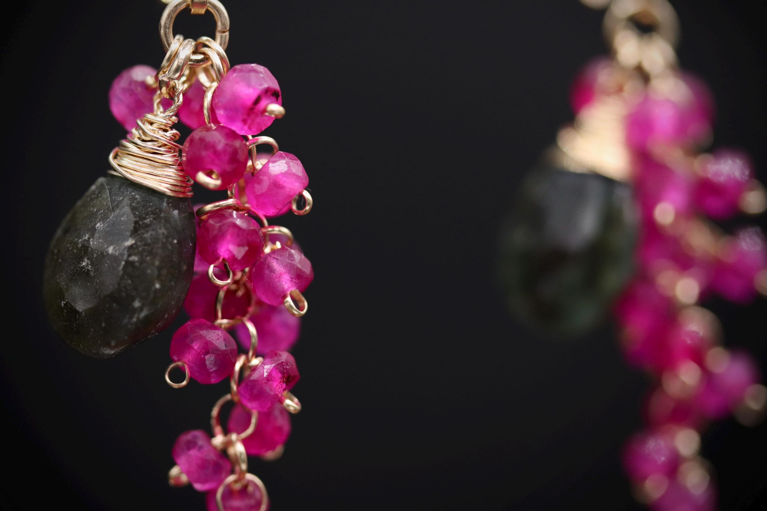 A close-up view of a pair of earrings with a dark stone and a cluster of pink gemstones.