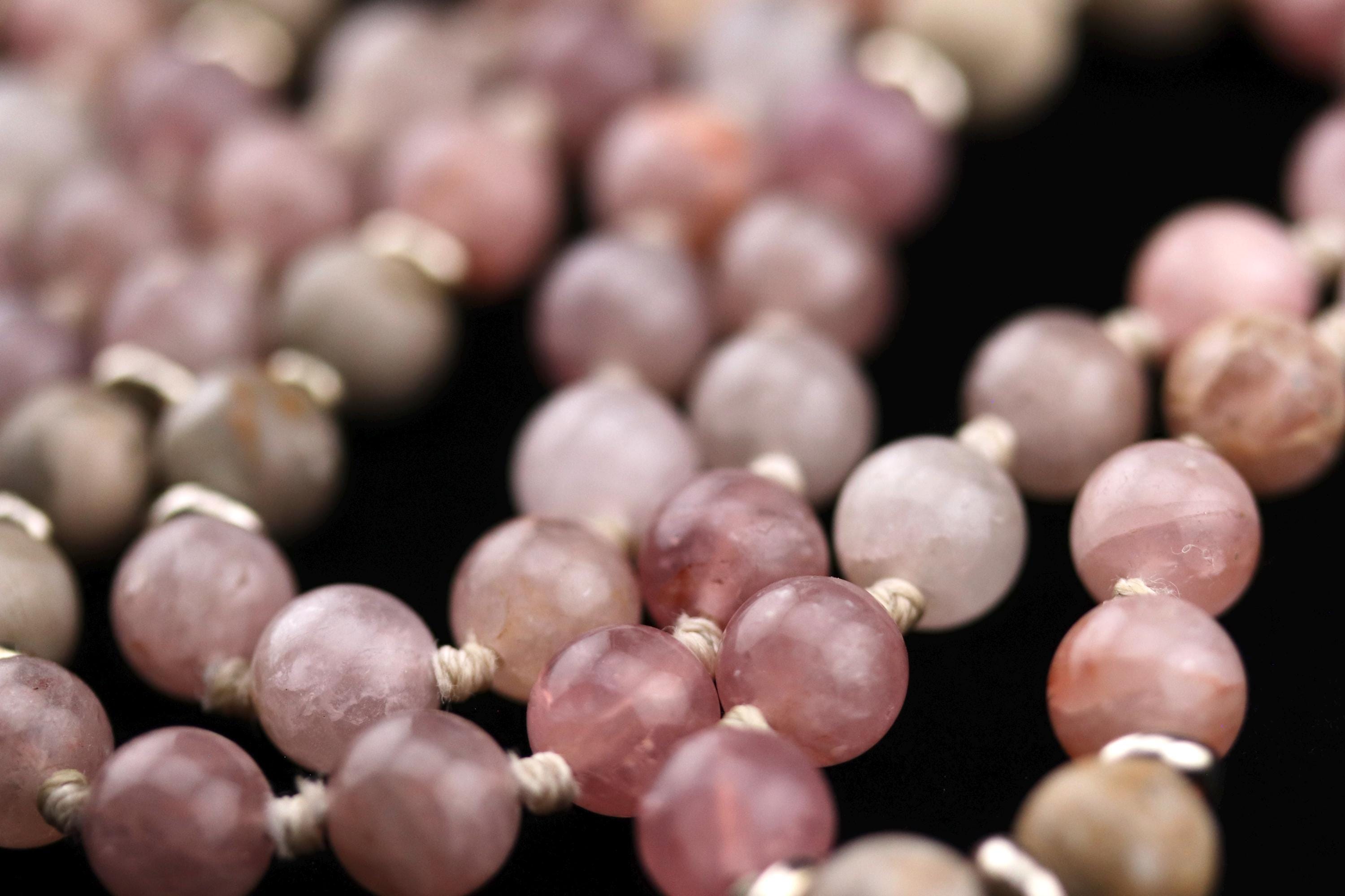 A close-up image of a collection of colorful beads, including pink, white, and gray stones, arranged in a pattern.