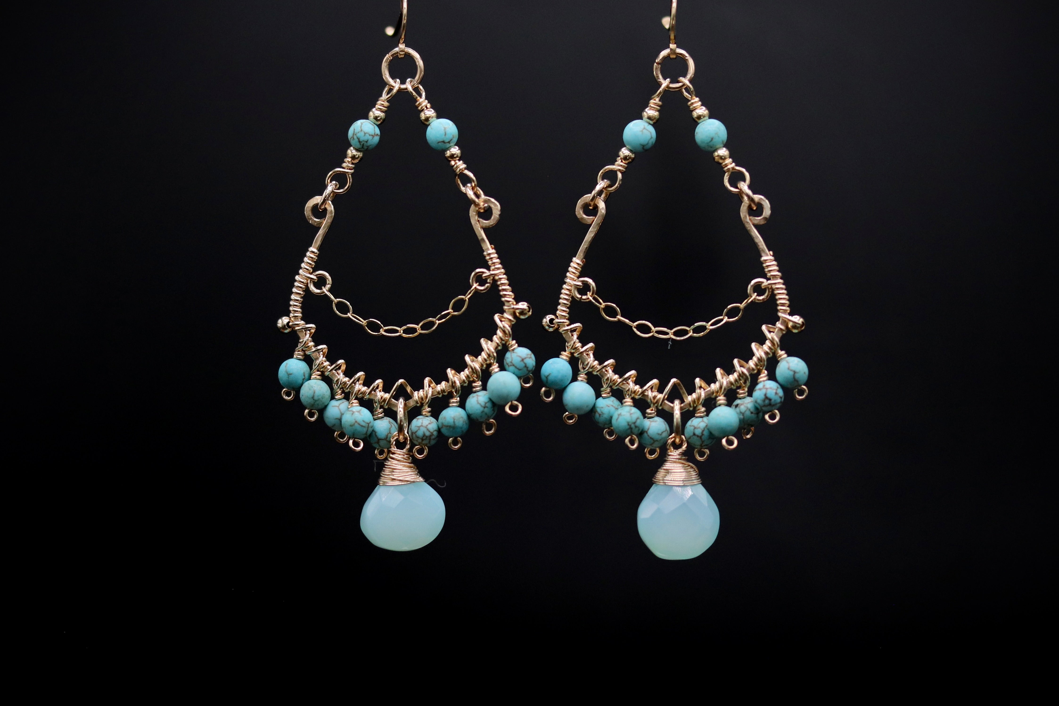 A pair of elegant earrings with turquoise stones and intricate metalwork, displayed against a black background.