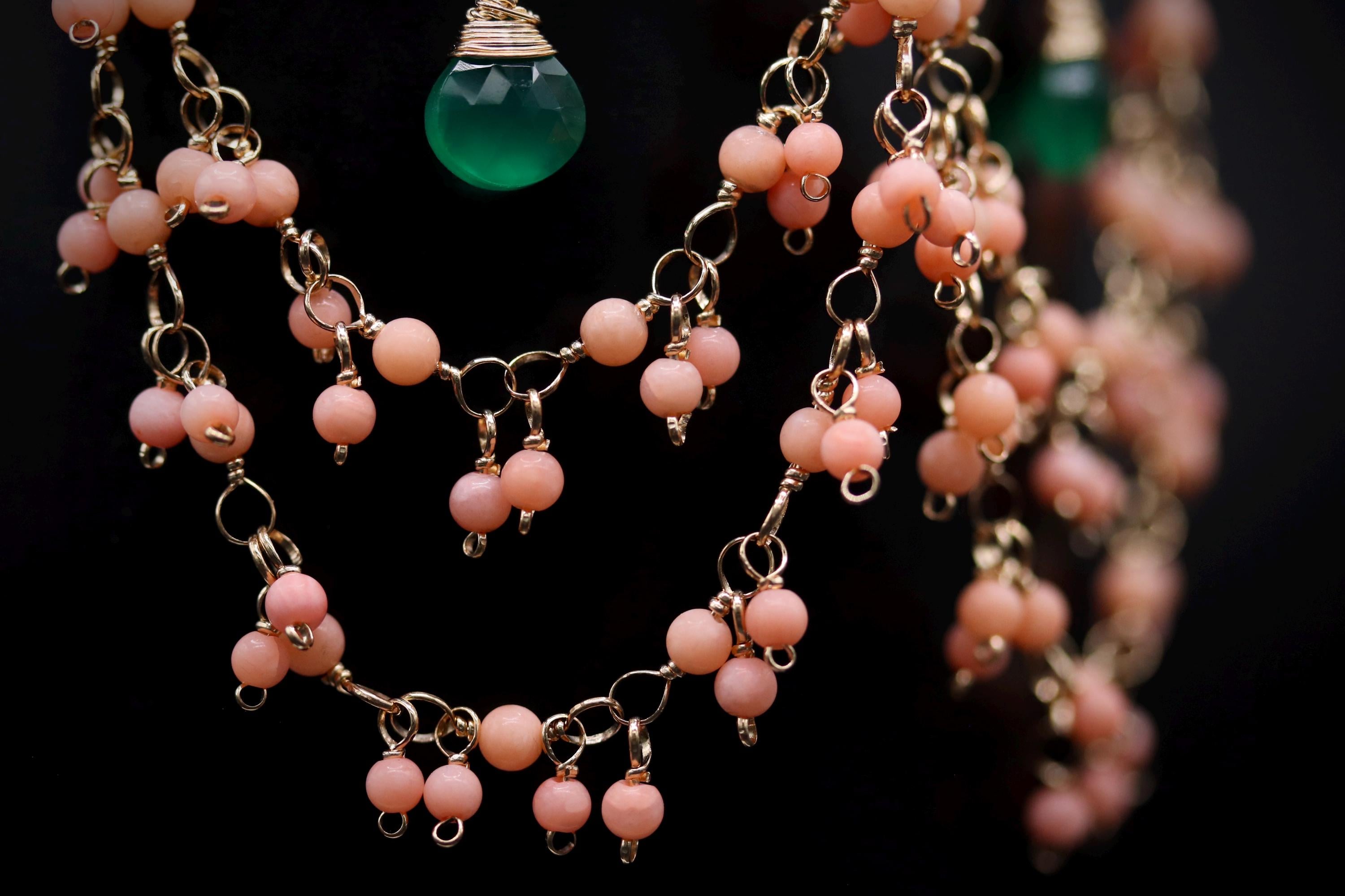 A close-up view of a necklace with multiple strands of beads in shades of pink and green, and a green pendant hanging from the top.