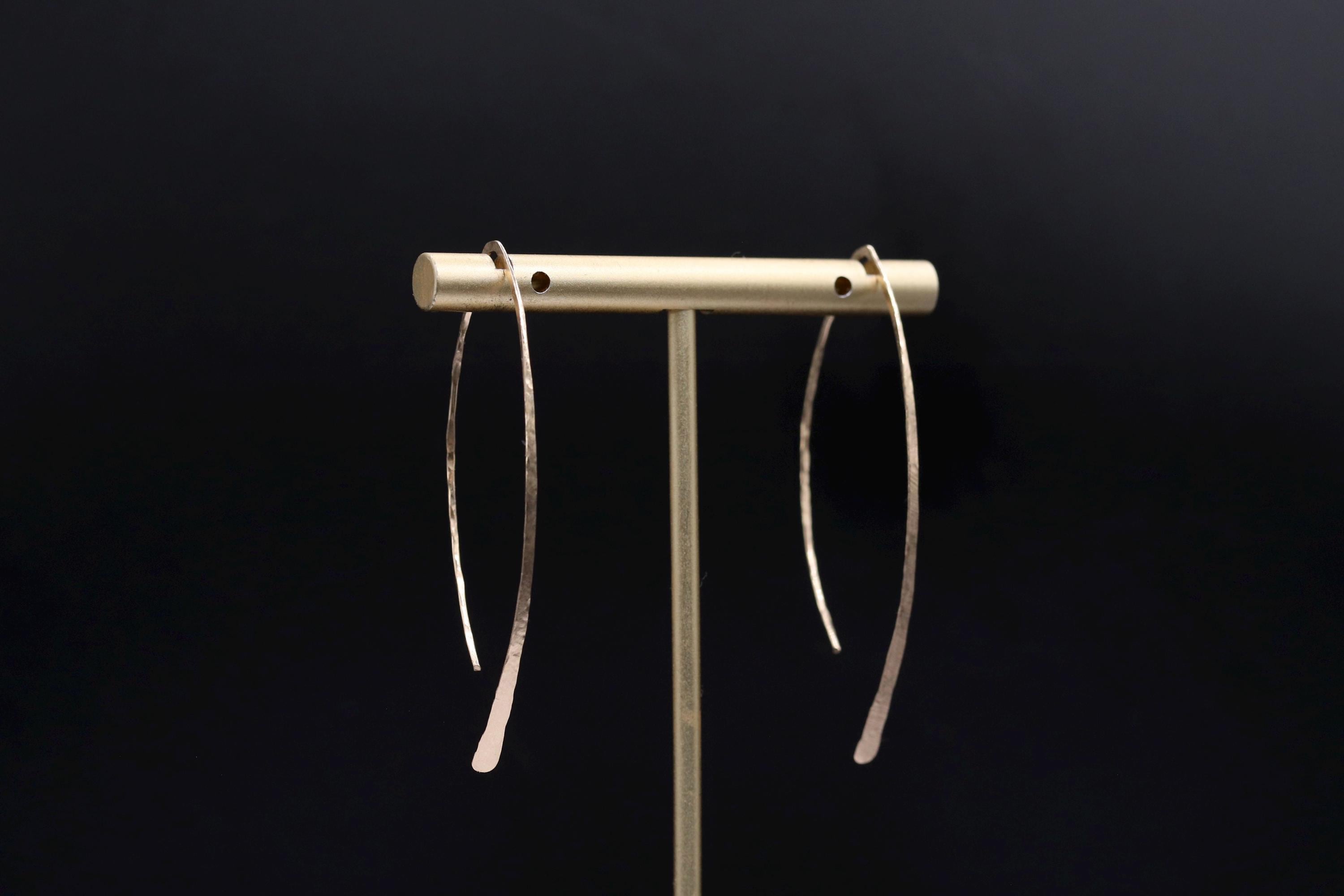 A pair of silver earrings with curved hooks is displayed on a stand against a dark background.